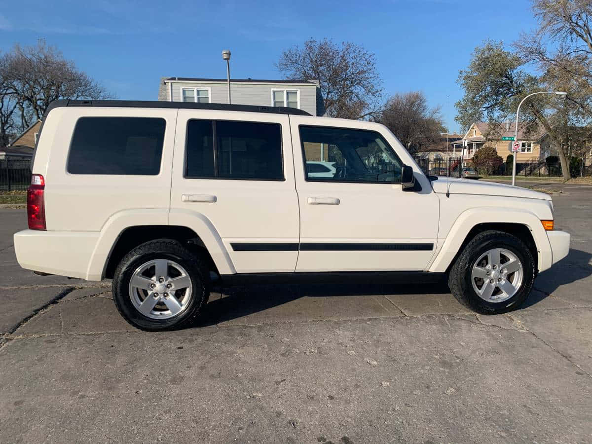 Jeep Commander 桌布 壁紙 — 一輛奶油色的Jeep Commander SUV停泊在破裂的瀝青路上，背景是晴朗的藍天、光禿的樹木和郊區房屋。