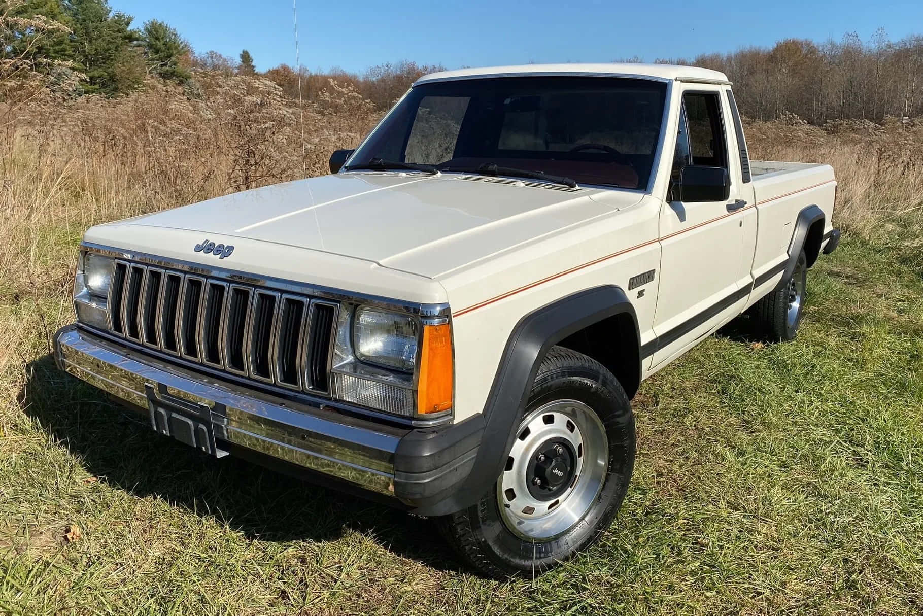 Jeep Comanche 桌布 壁紙 — 一輛奶油色的Jeep pickup貨車停泊在草地田野上，背景是晴朗的藍天和乾燥的蘆葦。