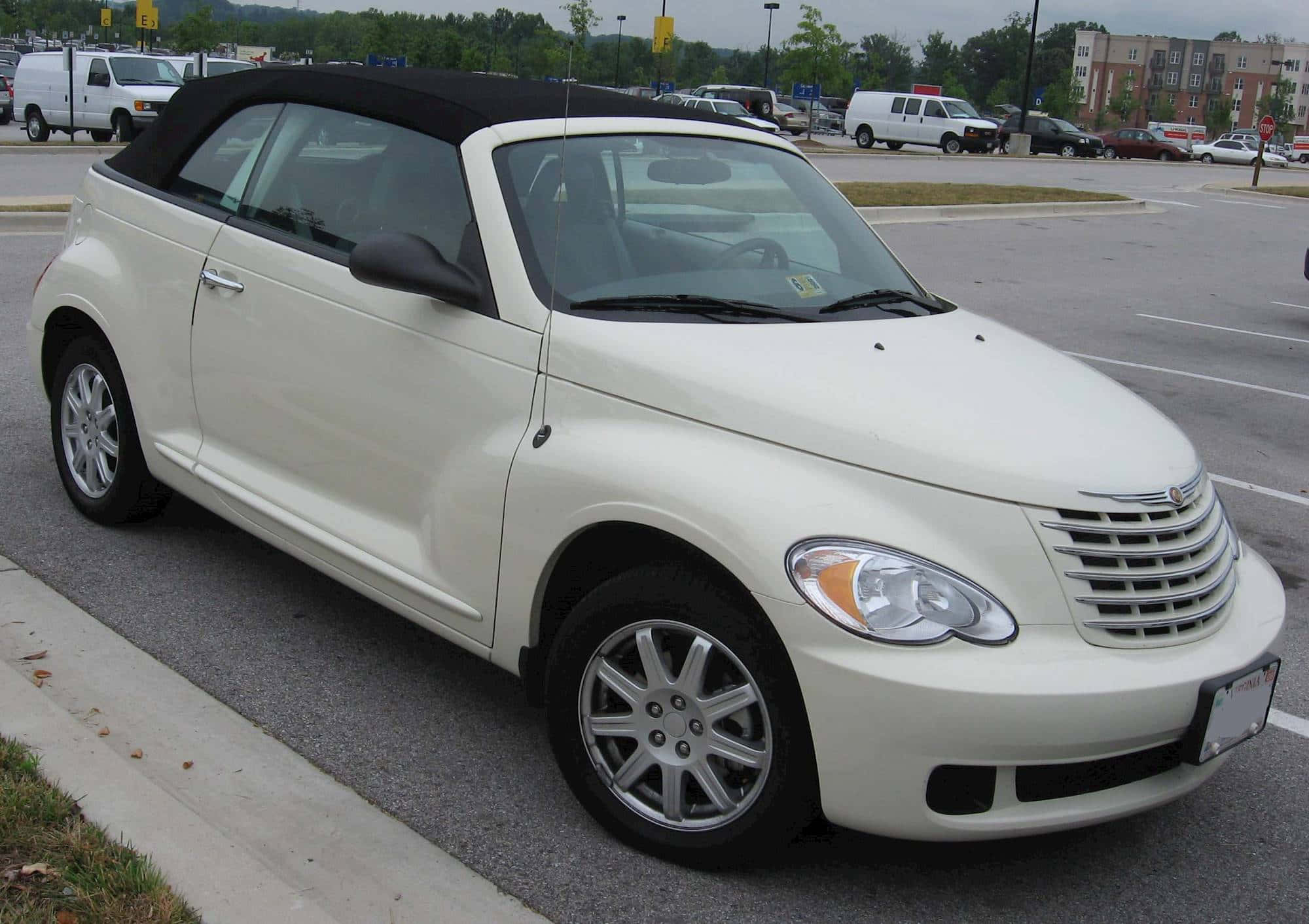 Chrysler Pt Cruiser 桌布 壁紙 — 一輛奶油色的PT Cruiser開篷車停泊在鋪砌的停車場，背景有樹木和建築物。