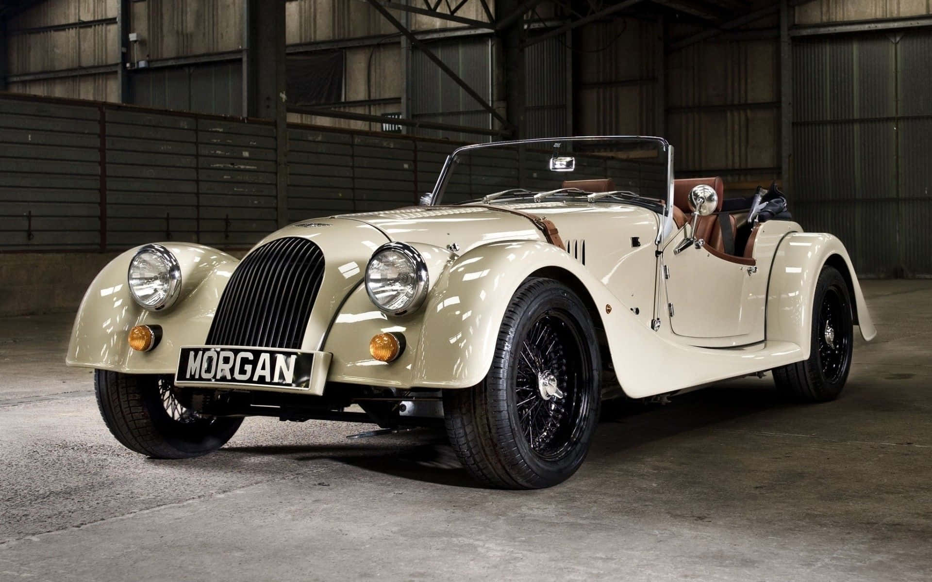 Morgan 桌布 壁紙 — 一輛奶油色經典摩根跑車配黑色鋼絲輪，優雅地停放在鄉村工業倉庫中。