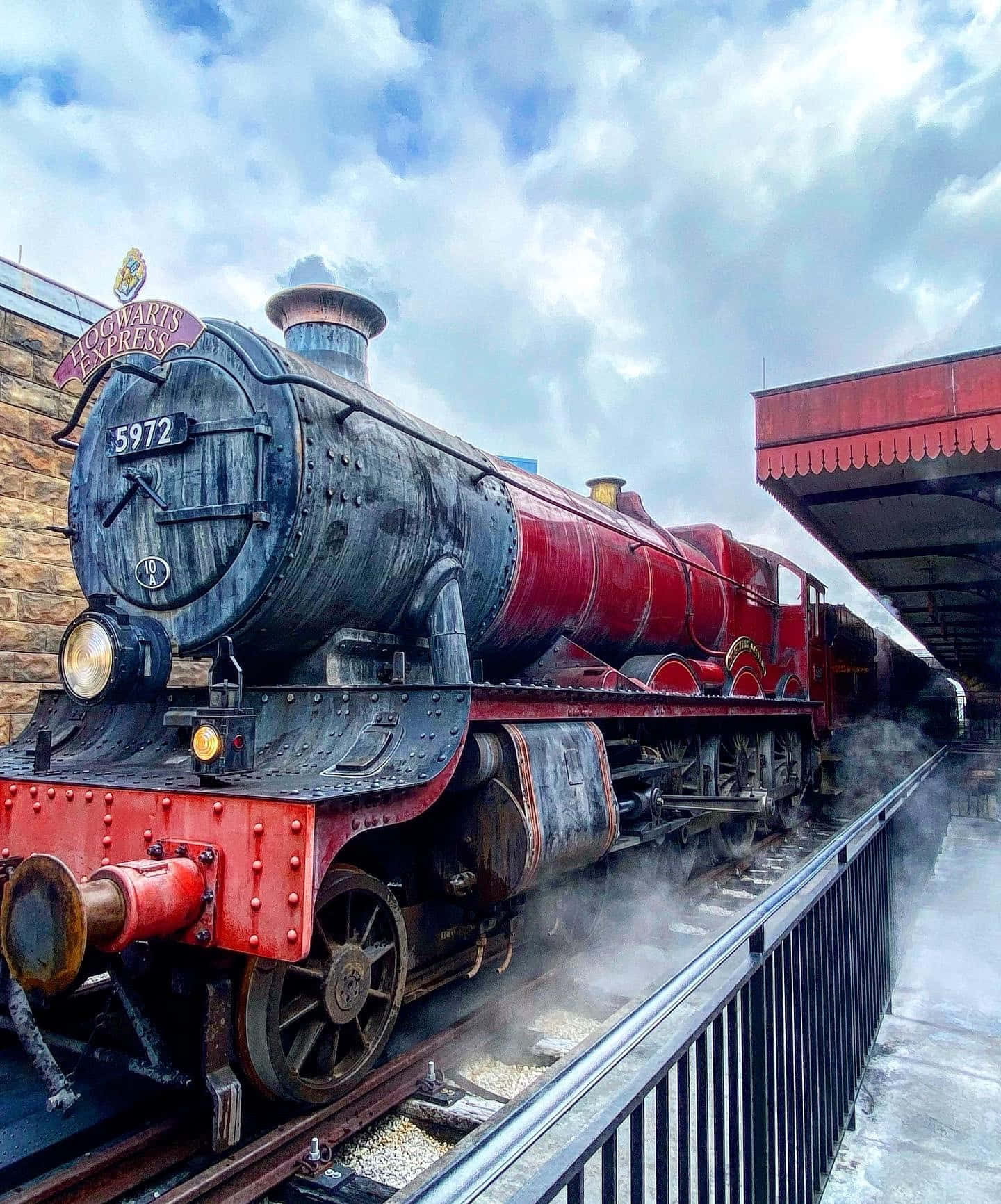 Hogwarts Express 桌布 壁紙 — 一輛宏偉的紅色和黑色霍格華茲特快蒸汽火車在陰天下的車站噴出蒸汽。