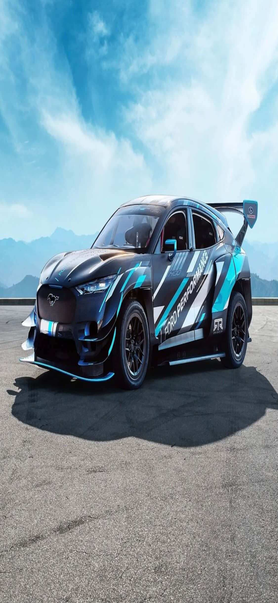 Ford F-150 GT RS - TRVS - TRVS - TRV 壁紙 — 一輛帶有 'Ford Performance' 貼紙的時尚黑色和藍綠色賽車停在鋪砌的道路上，背景是遠山和帶有薄雲的明亮藍天。