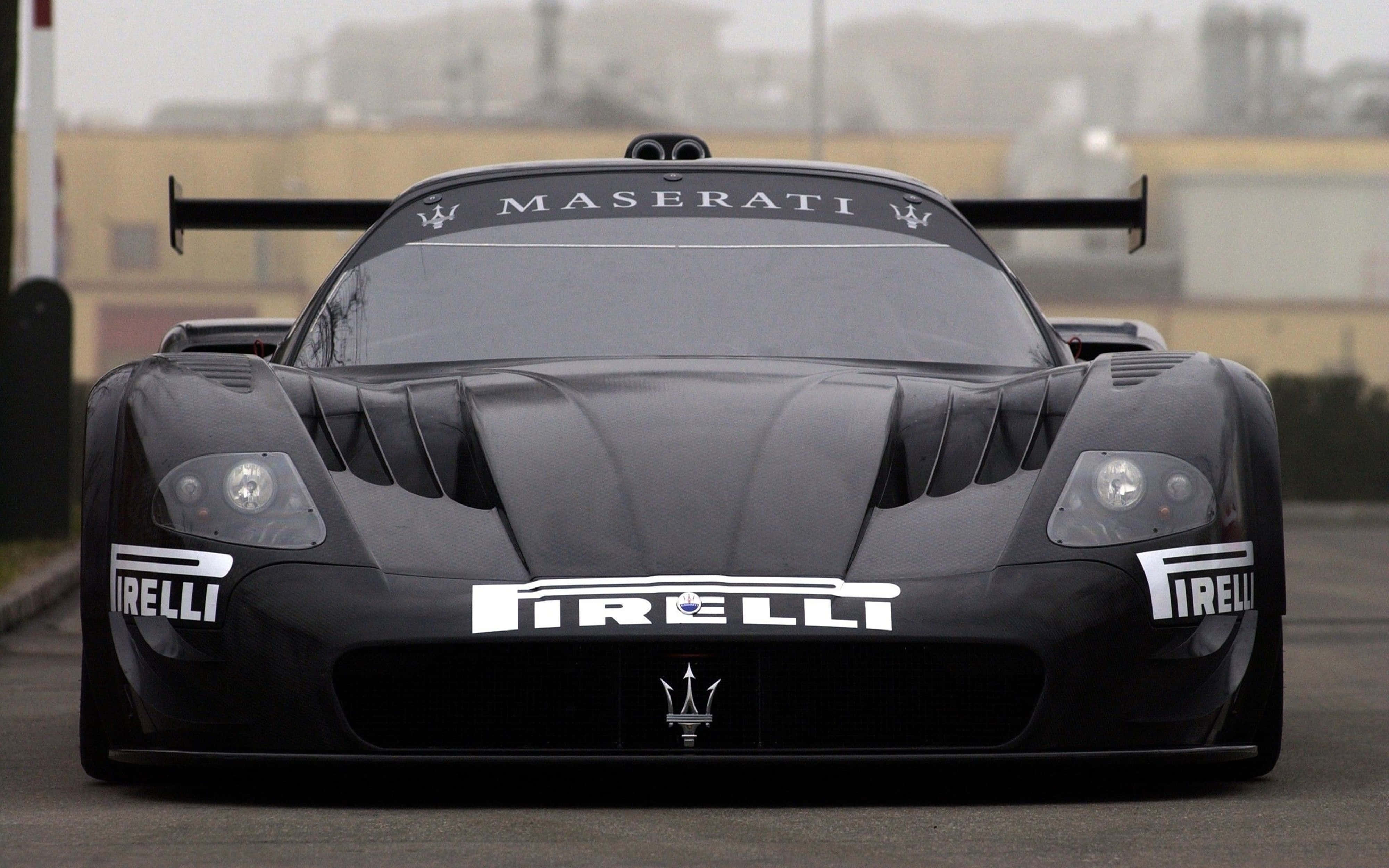 Pirelli Maserati 4K 壁紙 — 一輛帶有 Pirelli 品牌的時尚黑色 Maserati 賽車在陰天下的灰色瀝青賽道上向前行駛。