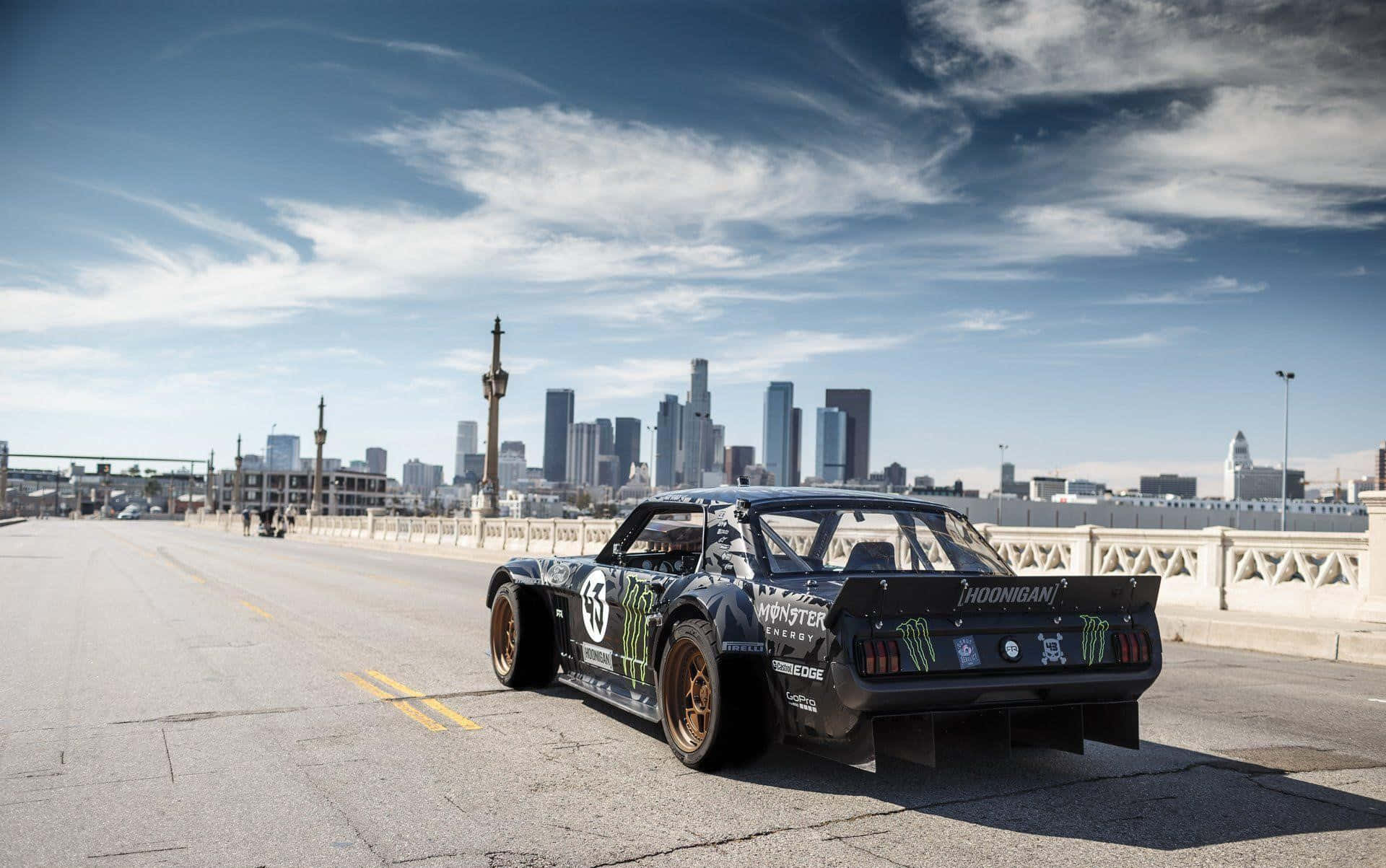 Hoonigan 桌布 壁紙 — 一輛帶有Monster Energy貼紙的黑色漂移車停在一座橋上，俯瞰著部分多雲藍天下城市天際線。
