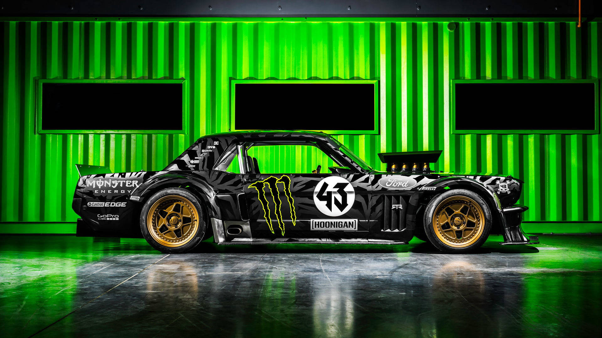 HD 桌布 壁紙 — 一輛帶有Monster Energy品牌標誌的黑金色漂移車，在光亮的車庫中，以充滿活力的綠色條紋牆壁為背景展示。