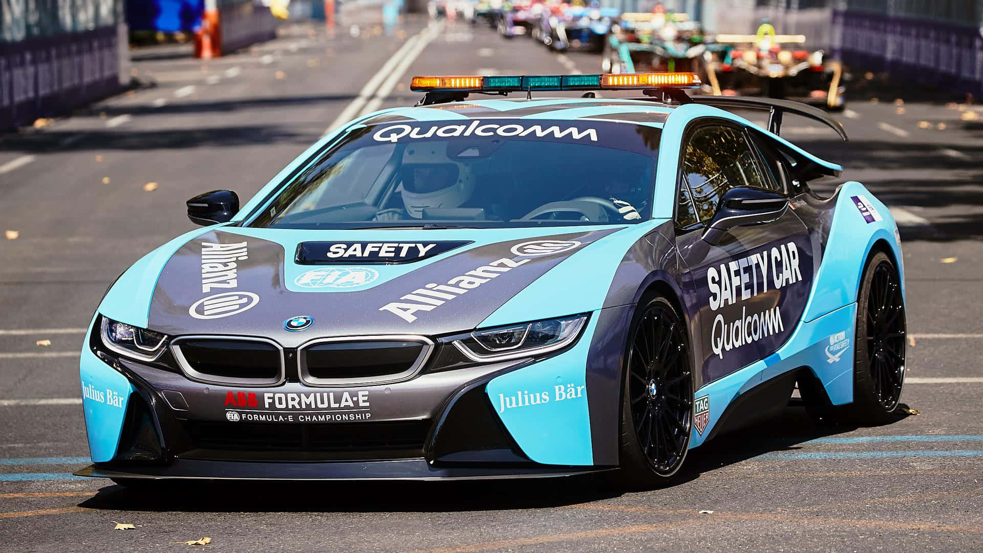 Safety Car 桌布 壁紙 — 一輛帶有Qualcomm和Allianz品牌標誌的藍灰色BMW i8安全車，在陽光明媚的街道賽道上引領Formula E比賽。