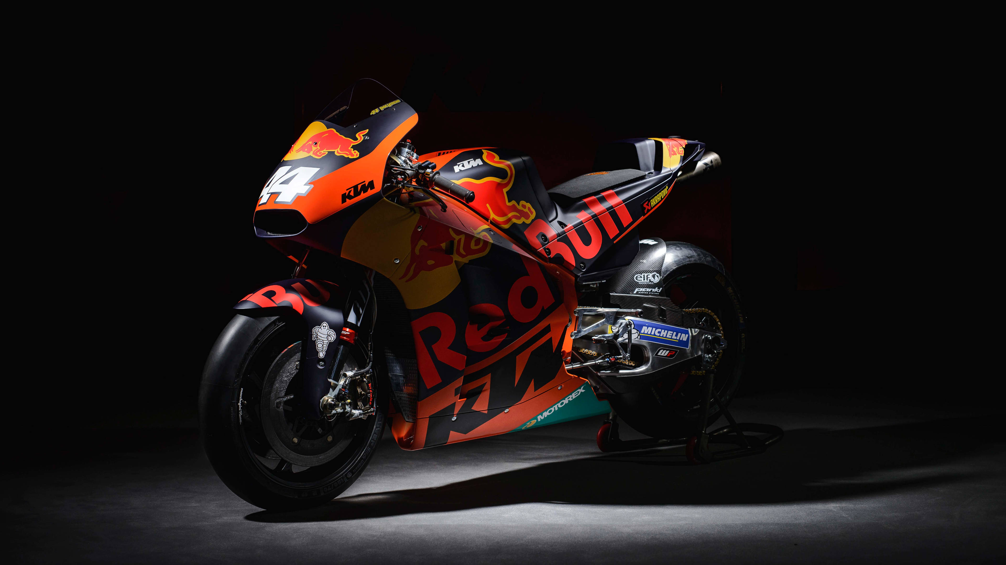 機車 桌布 壁紙 — 一輛帶有Red Bull品牌標誌的時尚KTM MotoGP電單車，在黑色背景下於戲劇性的攝影棚燈光中閃耀。