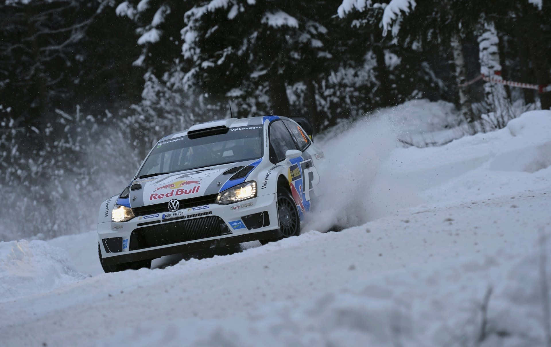 Ice Racing 桌布 壁紙 — 一輛帶有Red Bull標誌的白色福士偉根拉力賽車在雪地森林賽道上飛馳，激起雪花。