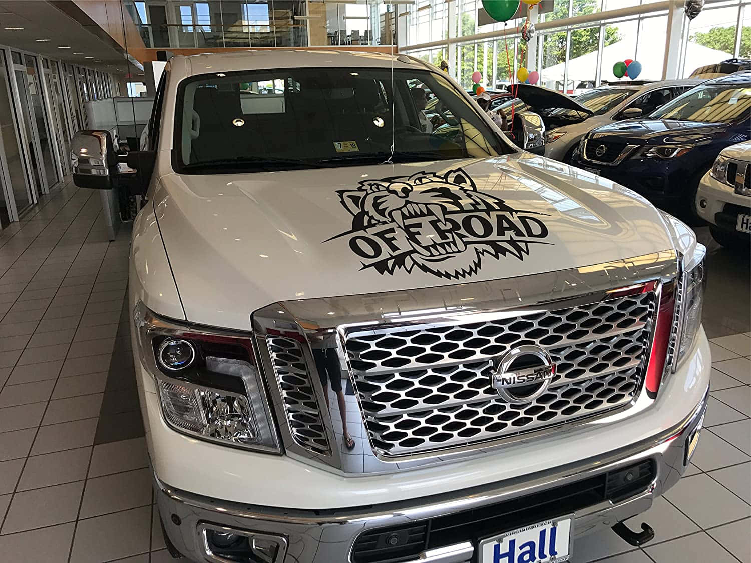 Car Hood 桌布 壁紙 — 一輛帶有兇猛老虎貼紙和「OFF ROAD」文字的白色日產皮卡車，在明亮的汽車經銷商展廳中佔據主導地位。
