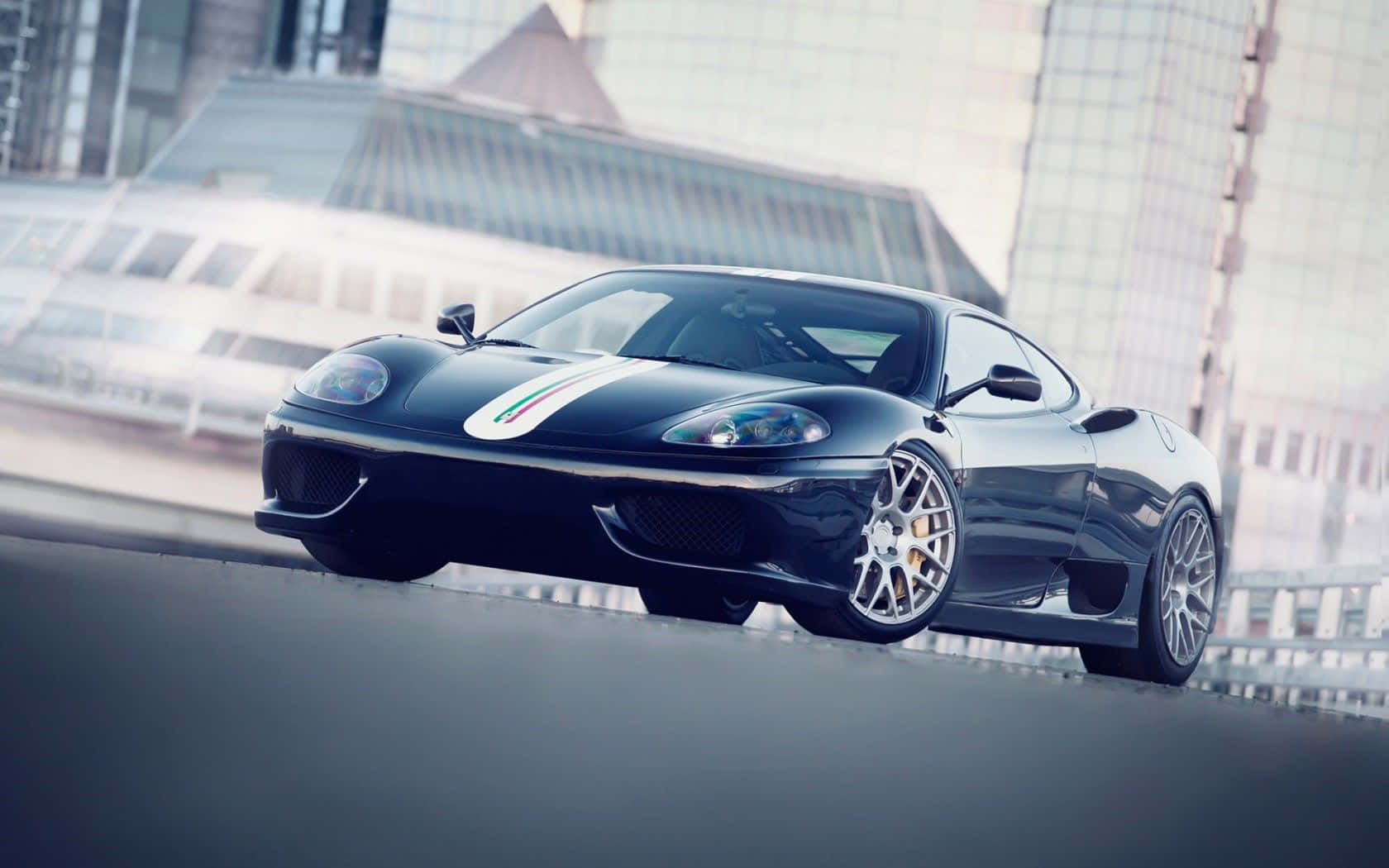 Ferrari 360 Modena 桌布 壁紙 — 一輛帶有意大利國旗條紋的時尚黑色法拉利跑車，在模糊的現代建築背景下，於城市街道上滑行。