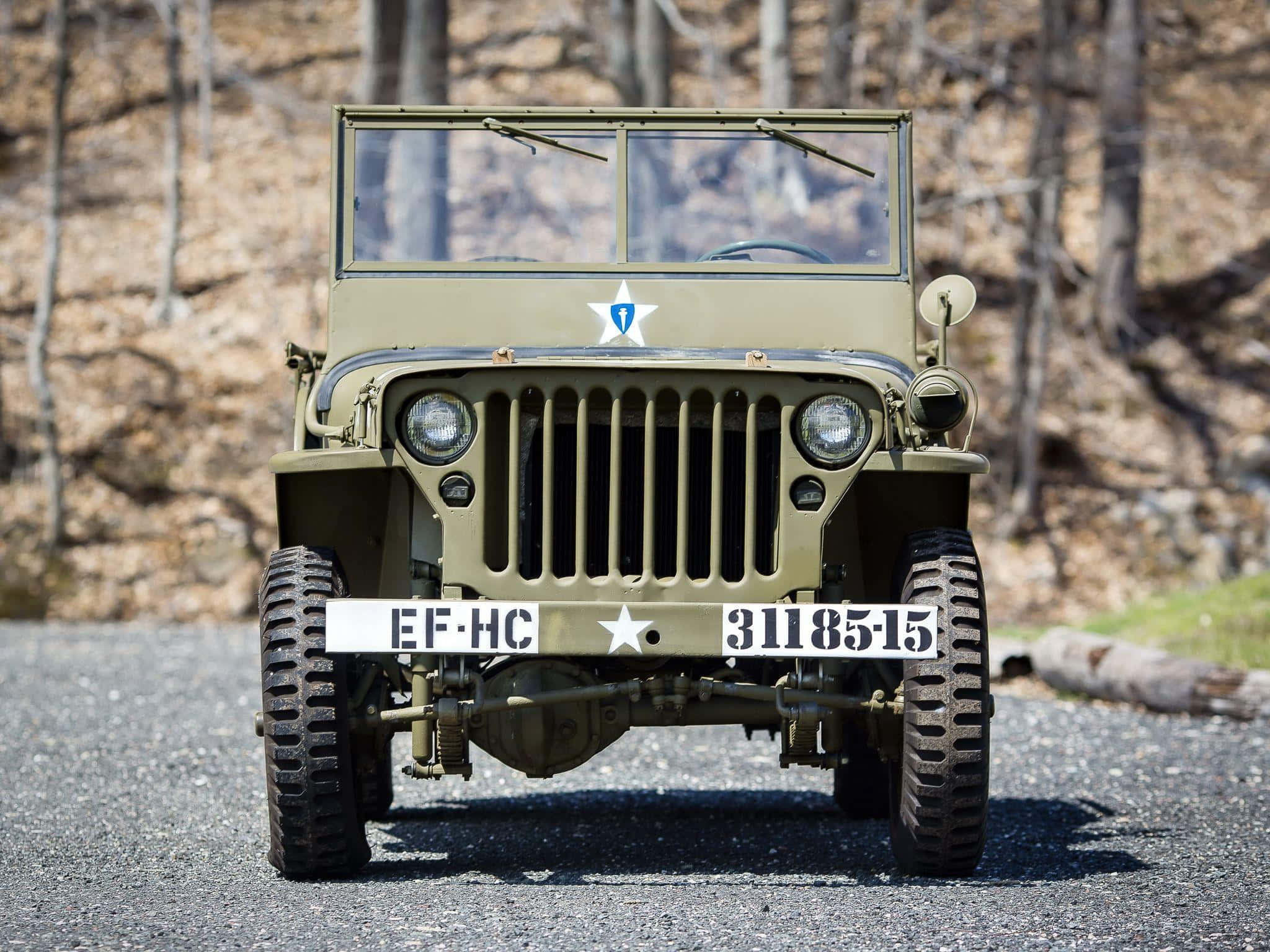 Jeep Gladiator 桌布 壁紙 — 一輛帶有星形徽章的復古橄欖綠軍用吉普車停在樹林地區的碎石路上。