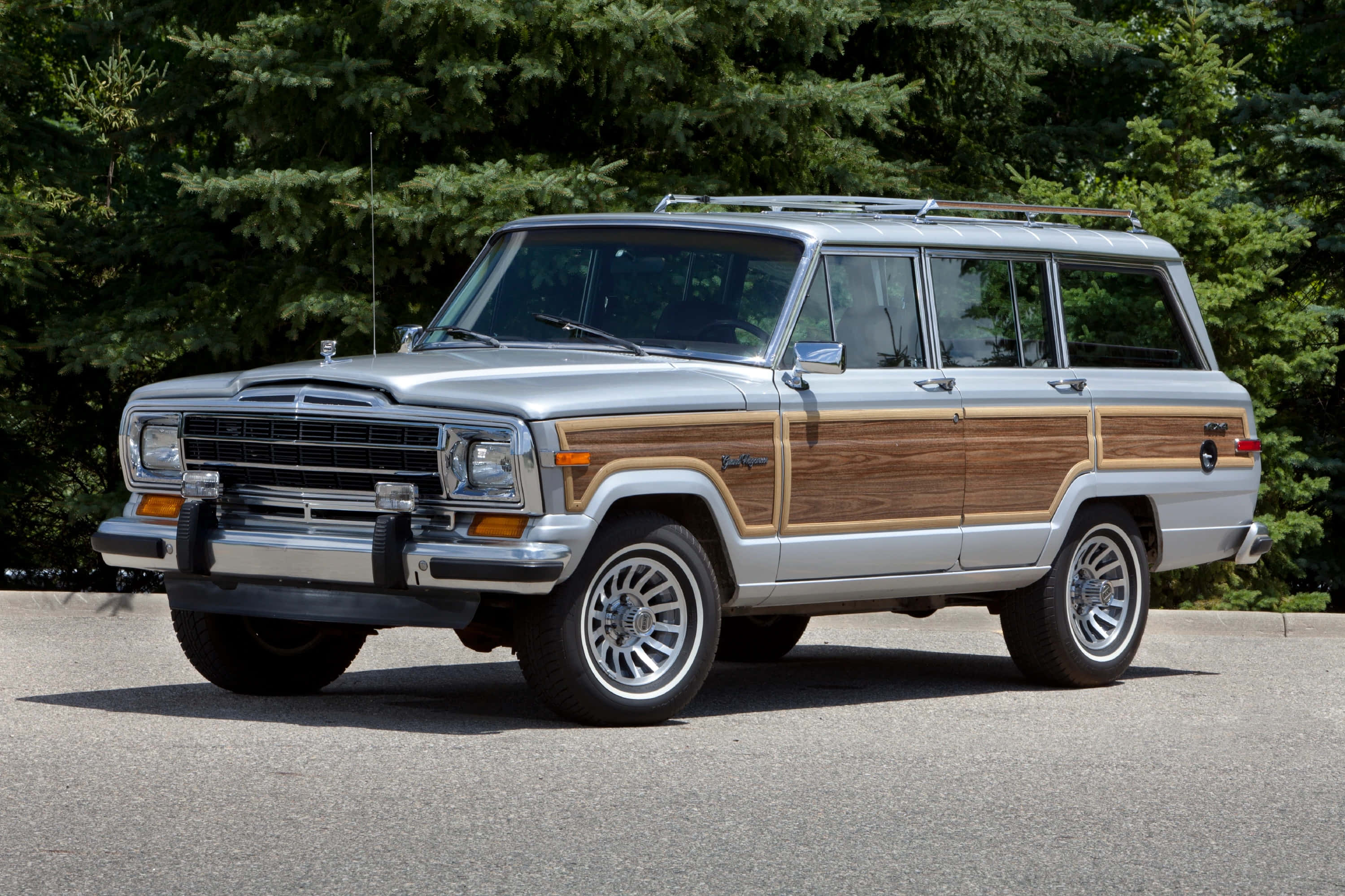 Jeep Wagoneer 桌布 壁紙 — 一輛帶有木飾板的銀色Jeep Wagoneer停泊在瀝青路上，周圍是茂密的綠樹。