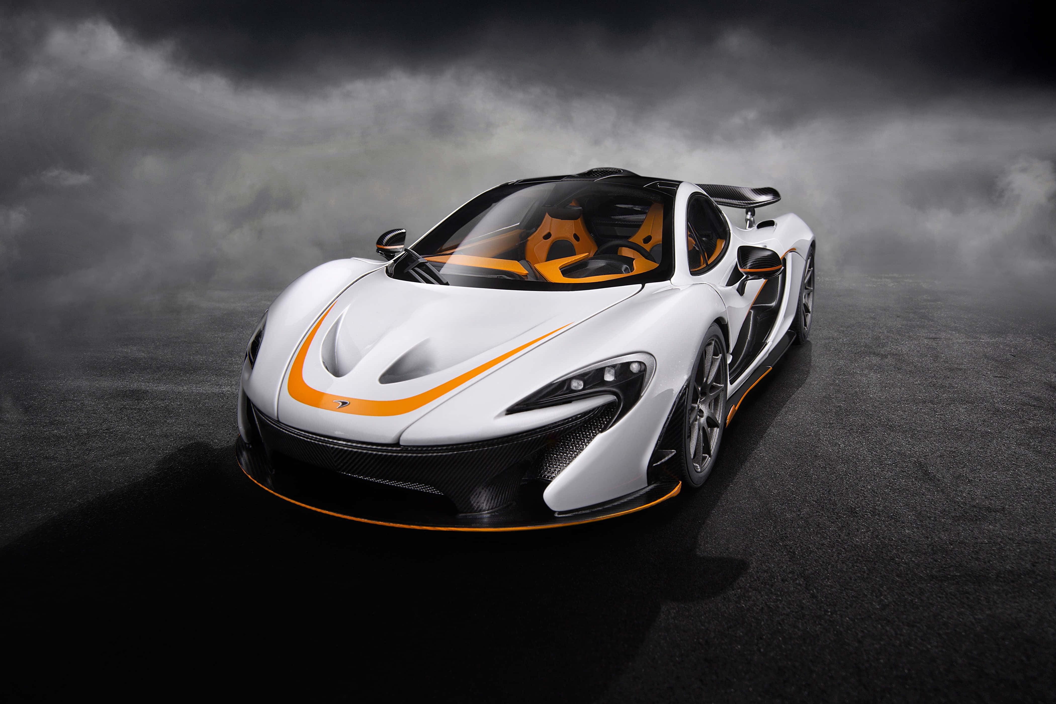 麥拿侖 桌布 壁紙 — 一輛帶有橙色點綴的白色McLaren跑車在黑暗潮濕的道路上，在戲劇性的暴風雲下閃閃發光。