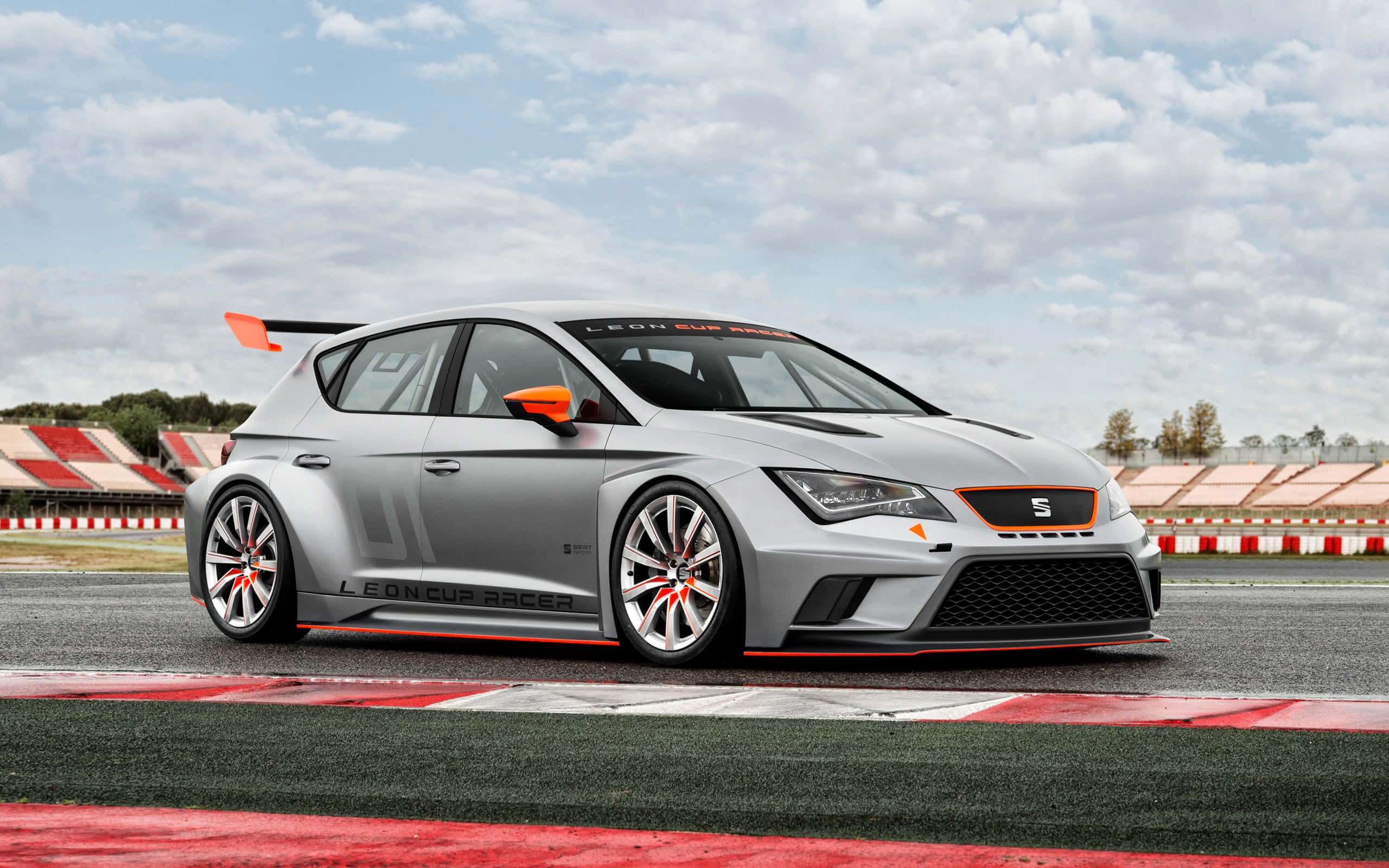 seat 桌布 壁紙 — 一輛帶有橙色點綴的銀色SEAT Leon Cup Racer在陰天下的賽道上蓄勢待發。