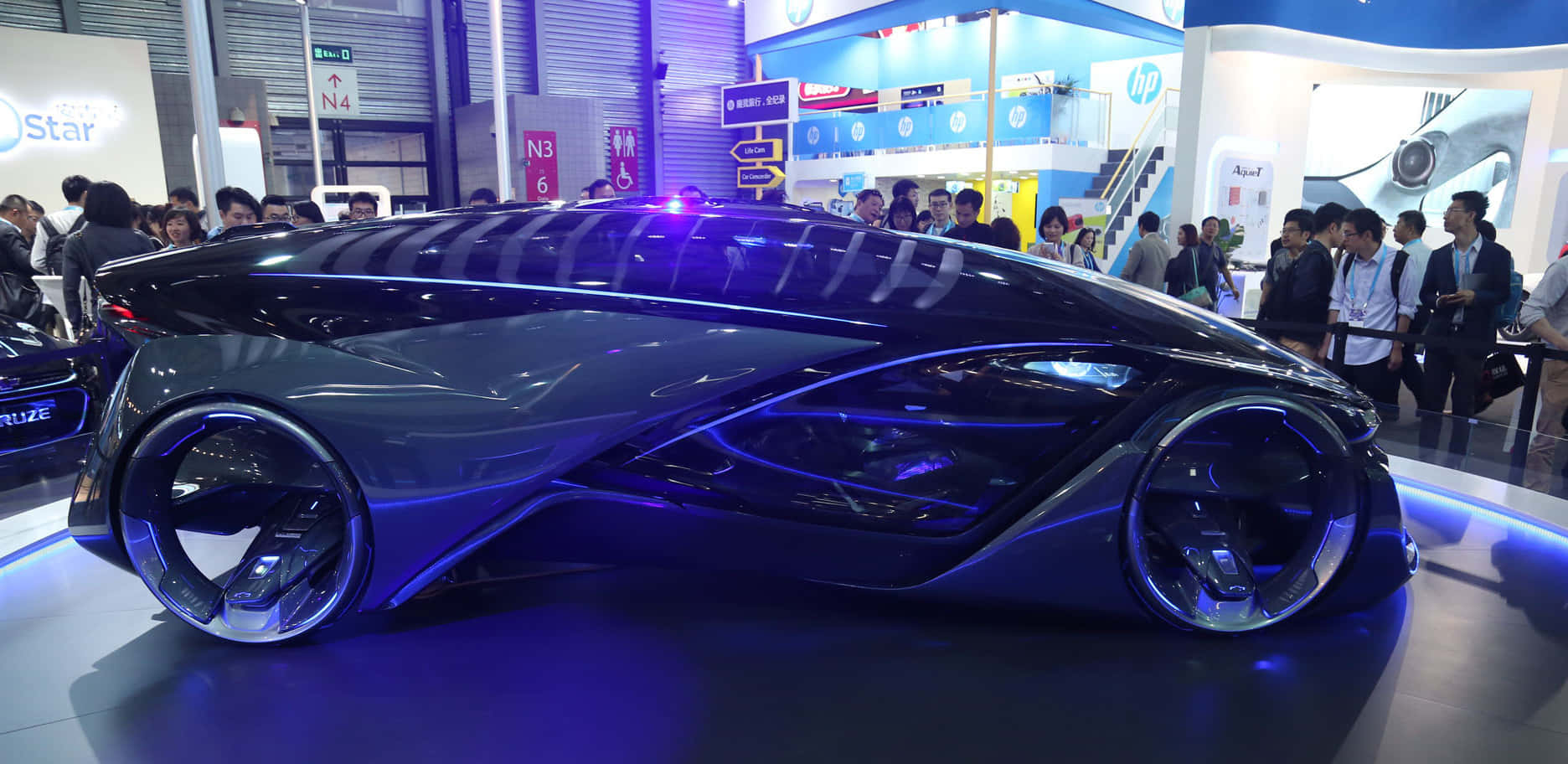 Car Technology 桌布 壁紙 — 一輛帶有發光藍色裝飾的時尚未來汽車在擁擠的科技展會上展出，與會者正在觀看。