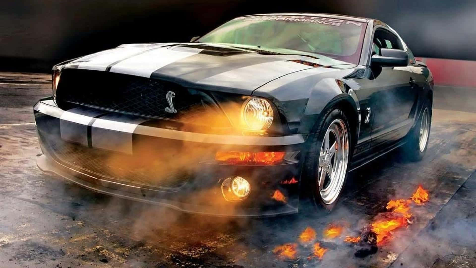 野馬 桌布 壁紙 — 一輛帶有白色條紋的黑色Shelby Mustang在戲劇性燈光下，在潮濕的賽道上燒胎並噴出火焰。