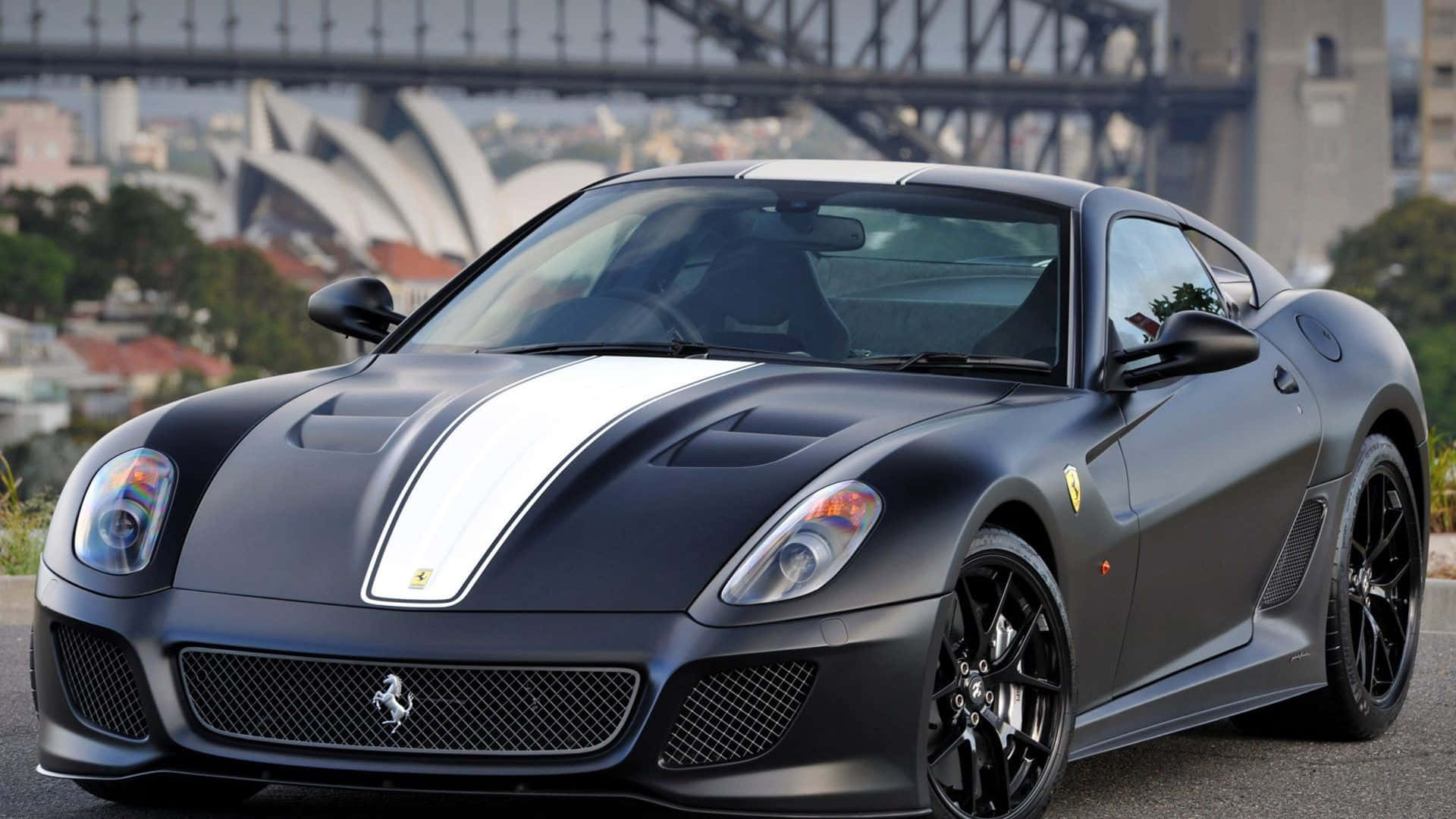 Ferrari 599 Gtb Fiorano 桌布 壁紙 — 一輛帶有白色賽車條紋的啞光黑色法拉利跑車停泊在悉尼歌劇院和港灣大橋前。