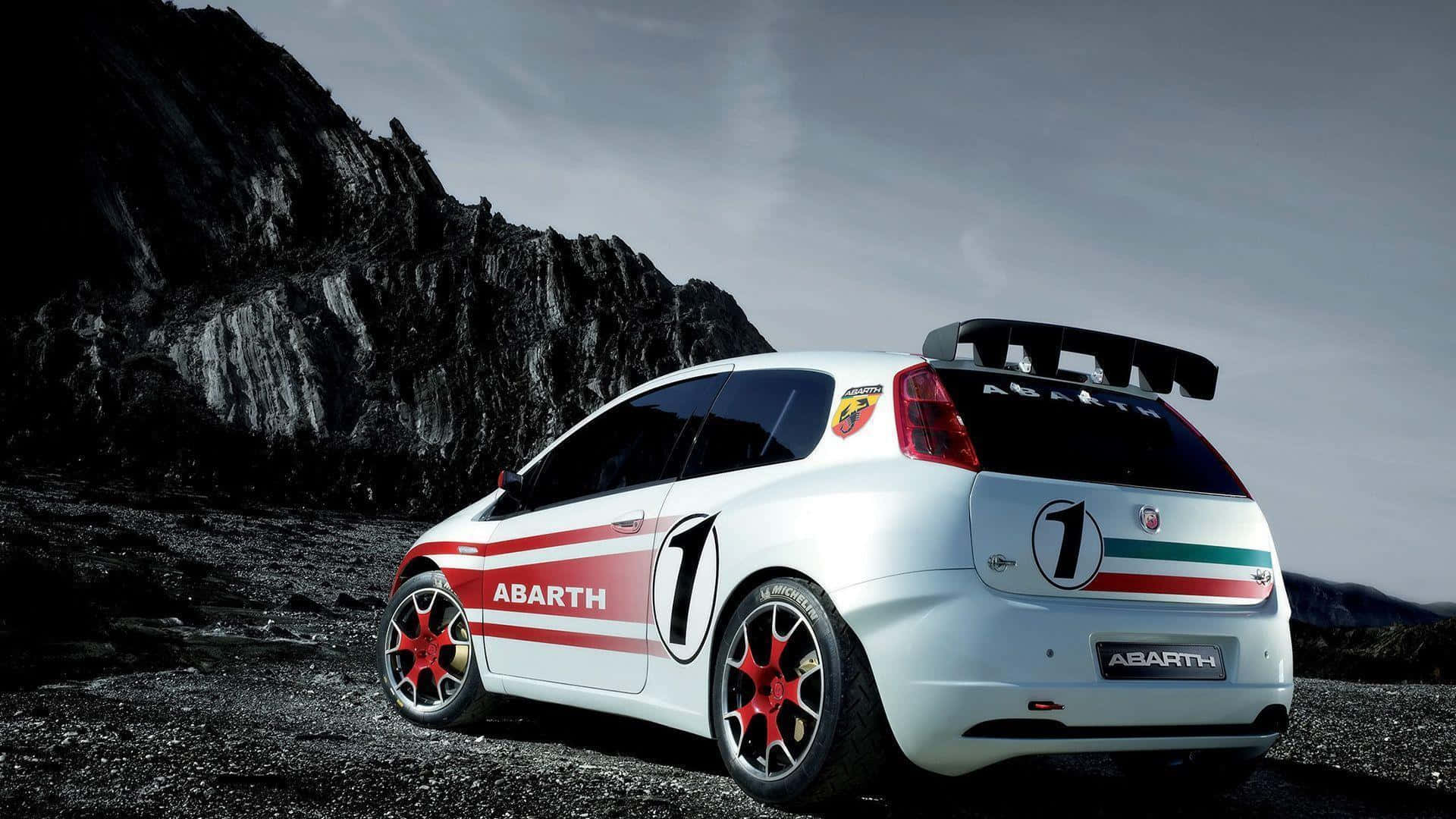 Abarth 桌布 壁紙 — 一輛帶有紅色點綴和1號貼紙的白色Abarth拉力賽車，停在岩石地形上，背景是壯麗的山脈。