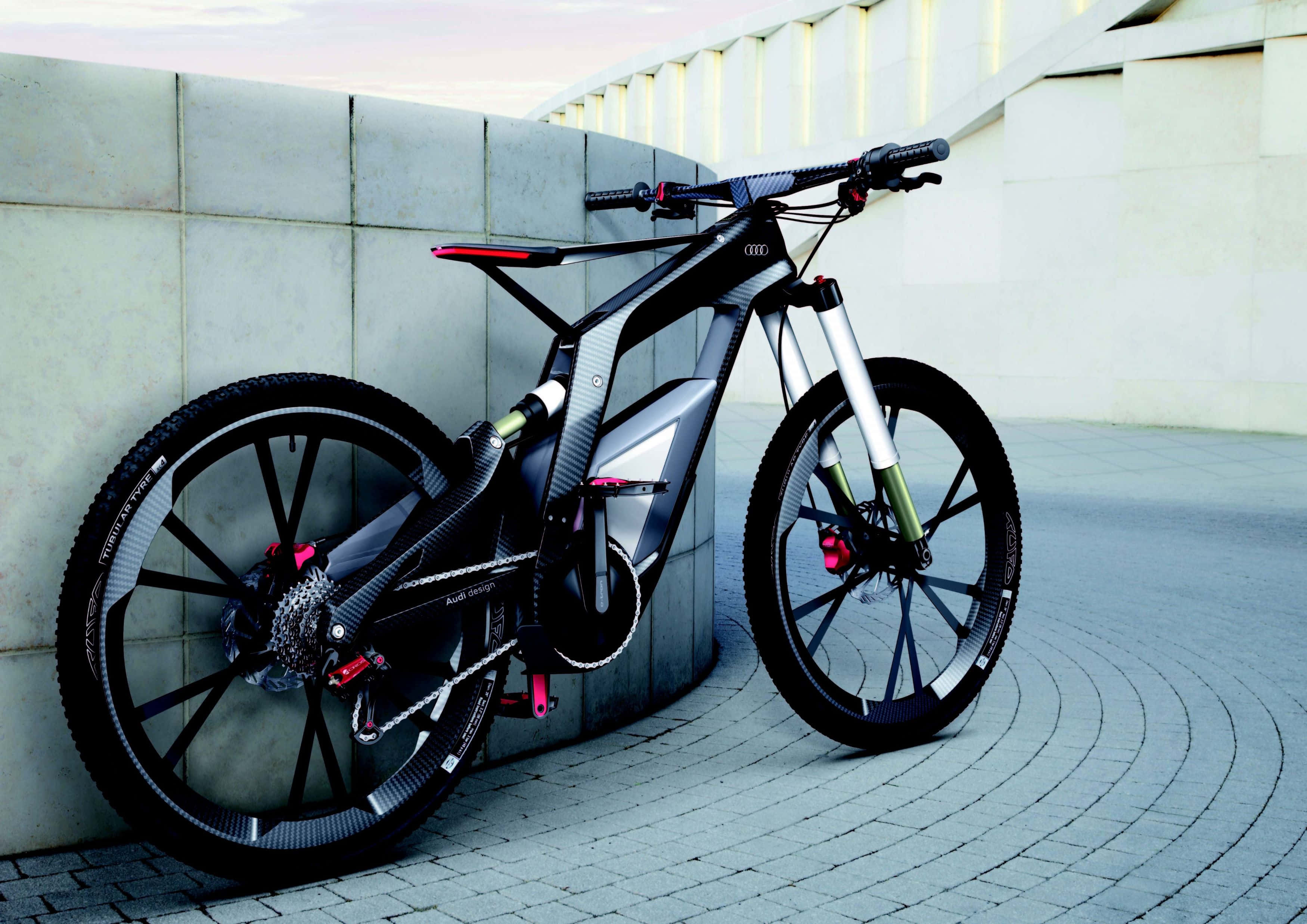 Electric Bike 桌布 壁紙 — 一輛帶有紅色點綴的時尚黑色Audi電動山地單車，在黃昏時靠在瓷磚廣場的弧形混凝土牆上。