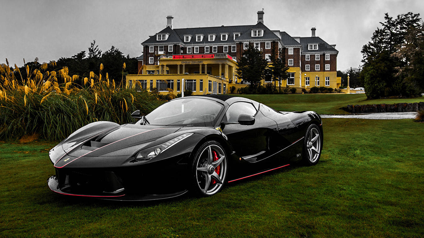 Sports Car 桌布 壁紙 — 一輛帶有紅色點綴的時尚黑色法拉利 LaFerrari 停放在修剪整齊的草坪上，前方是一座宏偉的黃色酒店，天空多雲。
