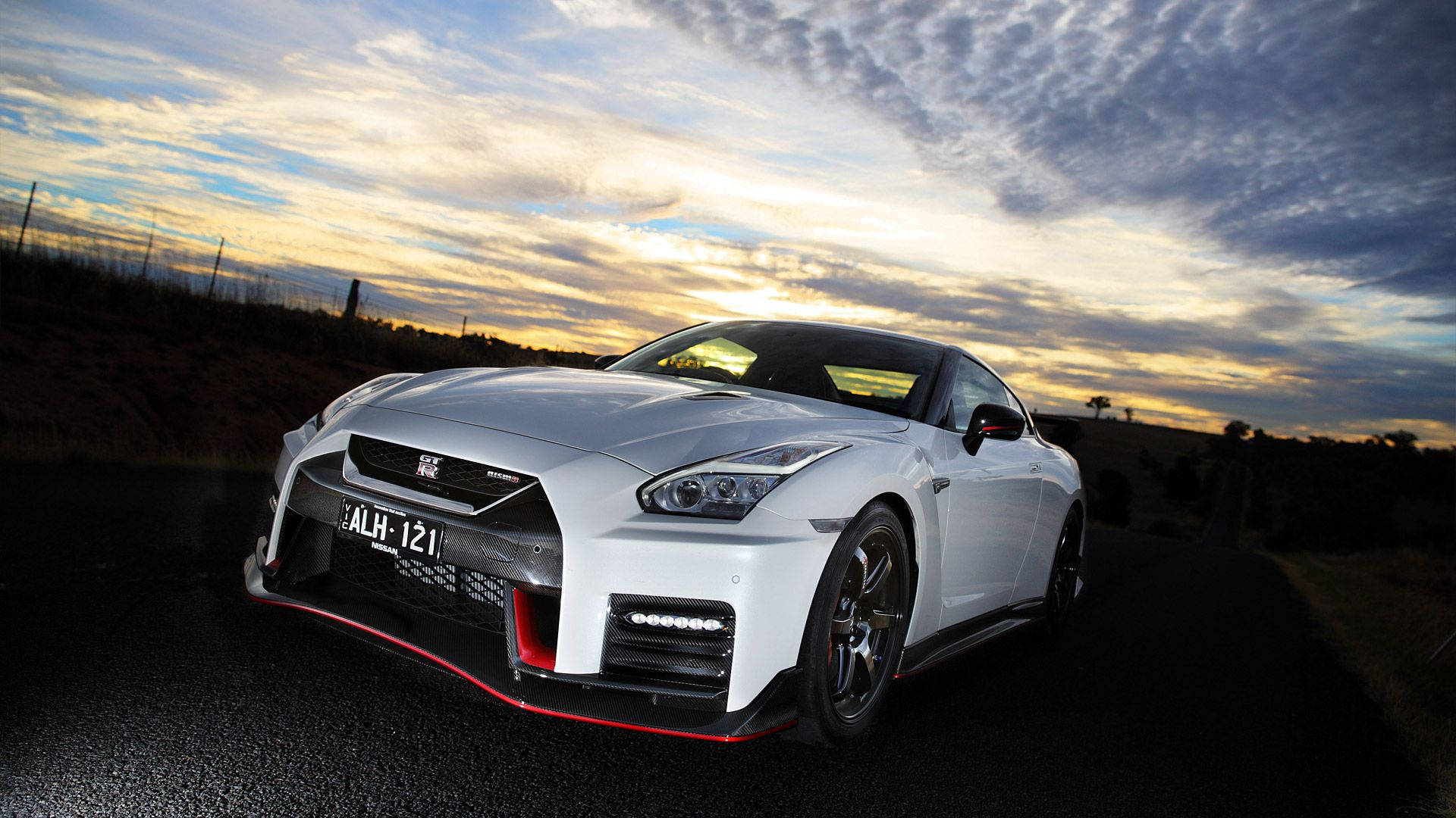 Nissan Nismo 壁紙 — 一輛帶有紅色點綴的白色日產GT-R跑車停在道路上，背景是戲劇性的日落天空。