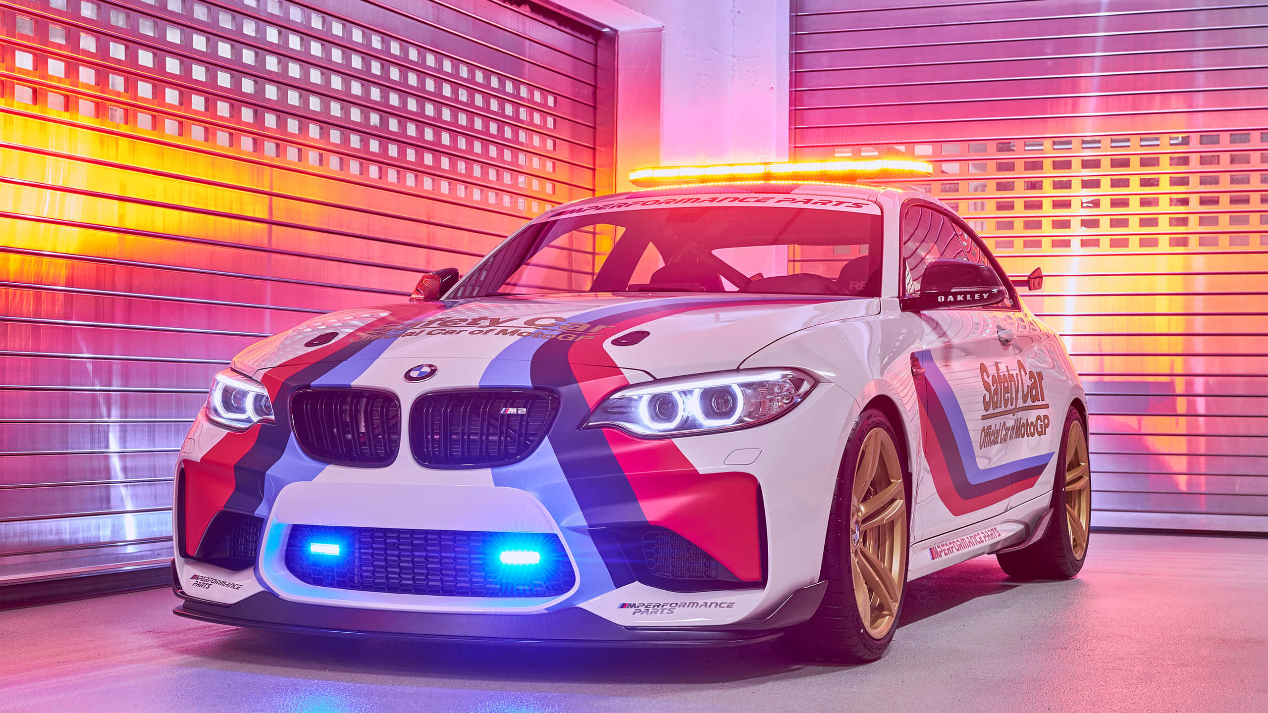 Safety Car 桌布 壁紙 — 一輛帶有紅藍條紋和發光燈光的白色BMW M2賽車，停在充滿活力粉橙色照明的車庫中。