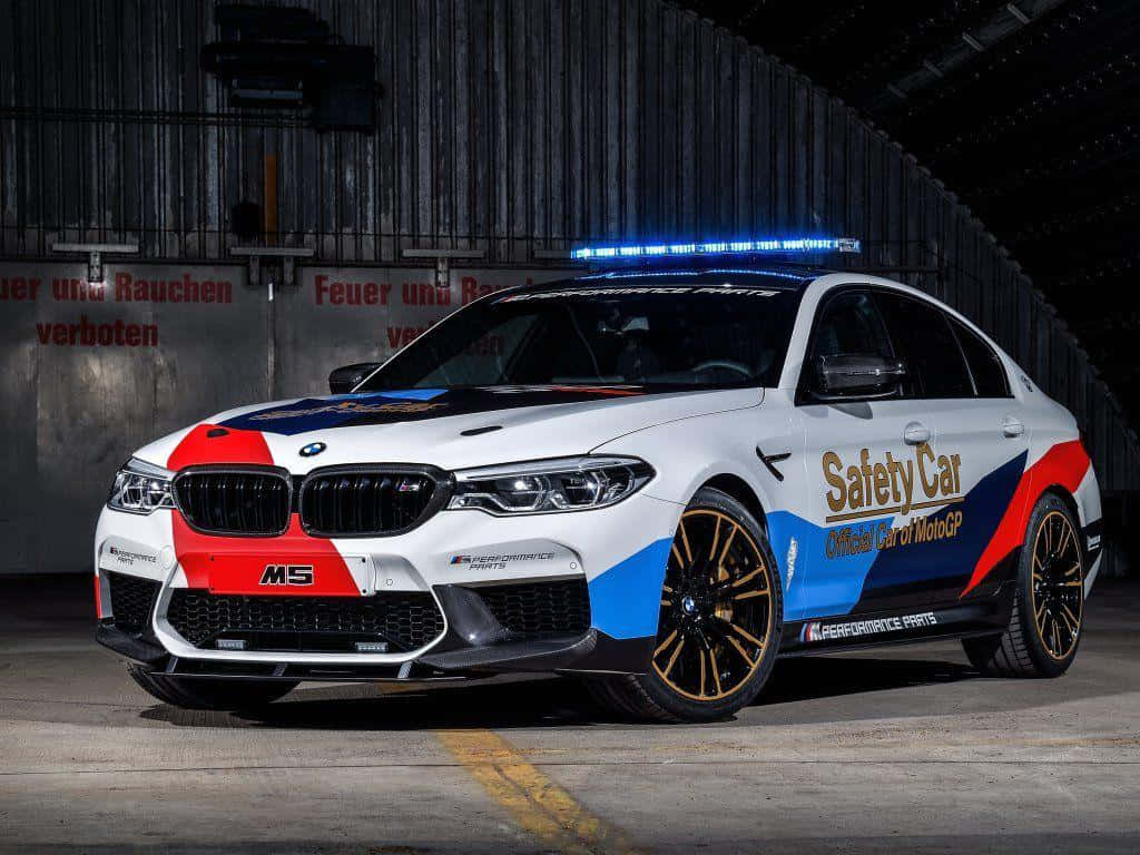 Safety Car 桌布 壁紙 — 一輛帶有藍、紅、黑塗裝的白色BMW M5安全車，在昏暗的車庫中閃爍著藍色燈光。