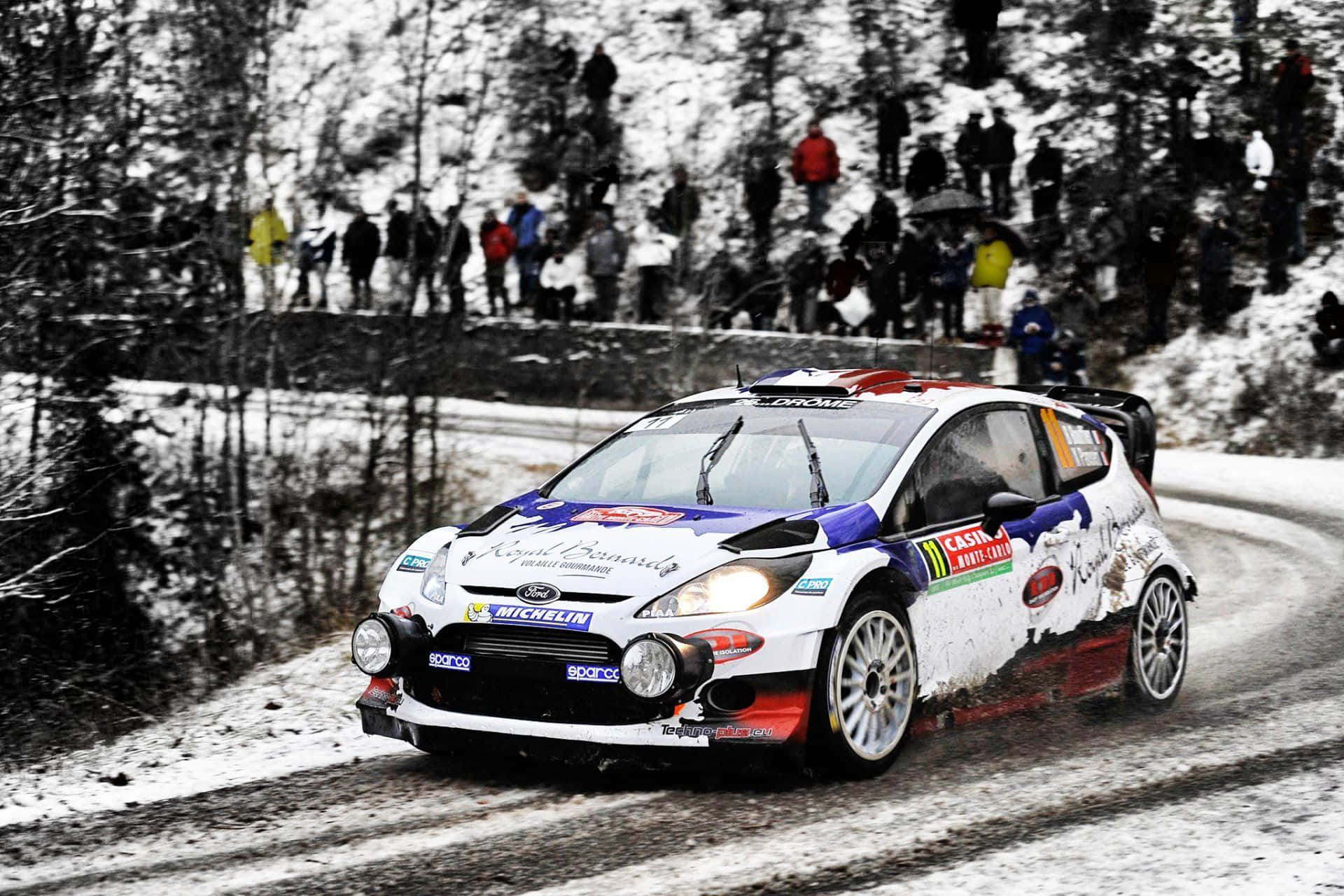 Ice Racing 桌布 壁紙 — 一輛帶有藍紅點綴的白色拉力賽車在積雪蜿蜒的森林道路上飛馳，觀眾在積雪的堤岸上觀看。
