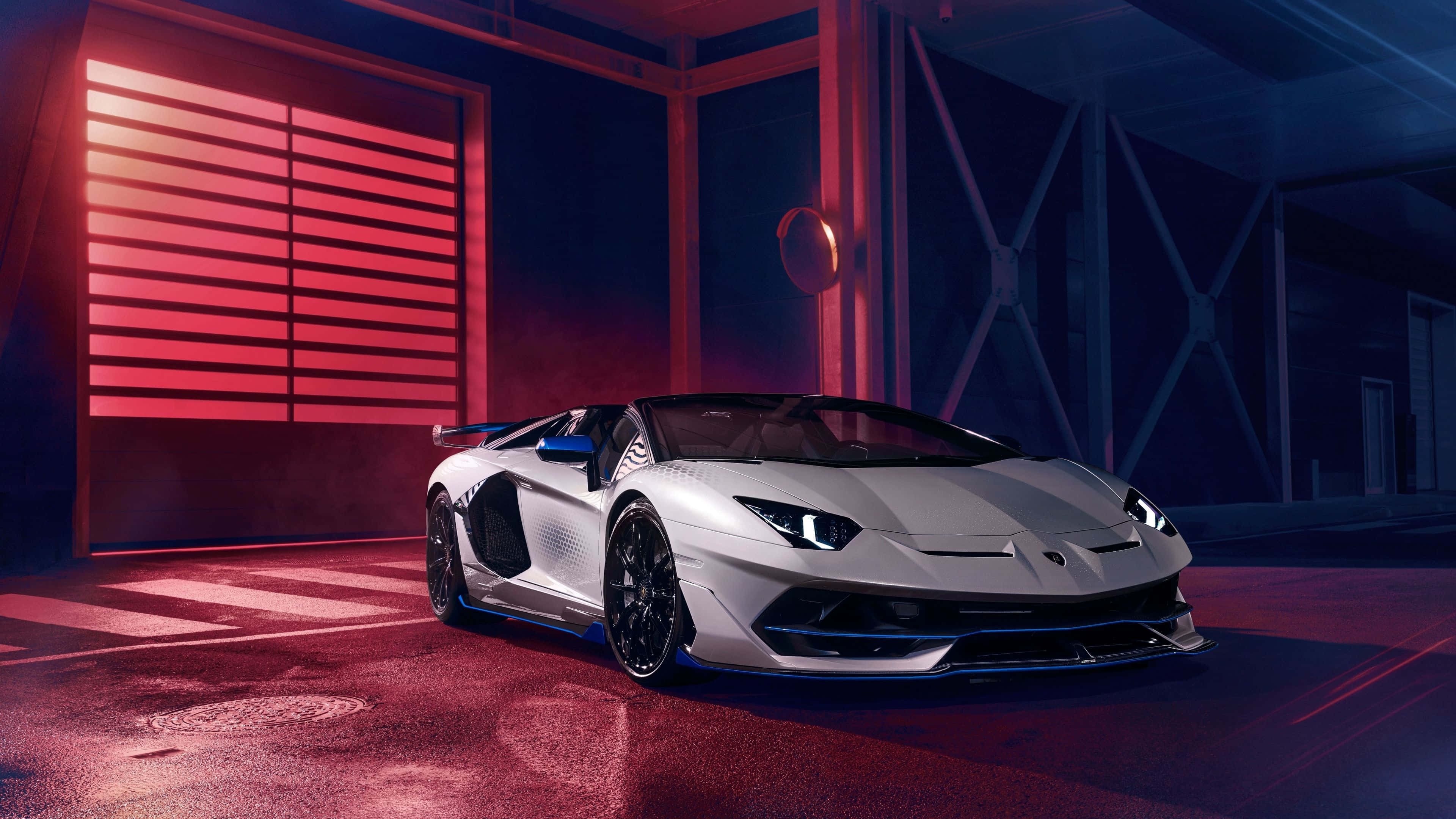 林寶堅尼 4K 桌布 壁紙 — 一輛帶有藍色點綴的時尚銀色林寶堅尼 Aventador SVJ 在現代車庫中，於戲劇性的紅色和藍色燈光下閃耀。