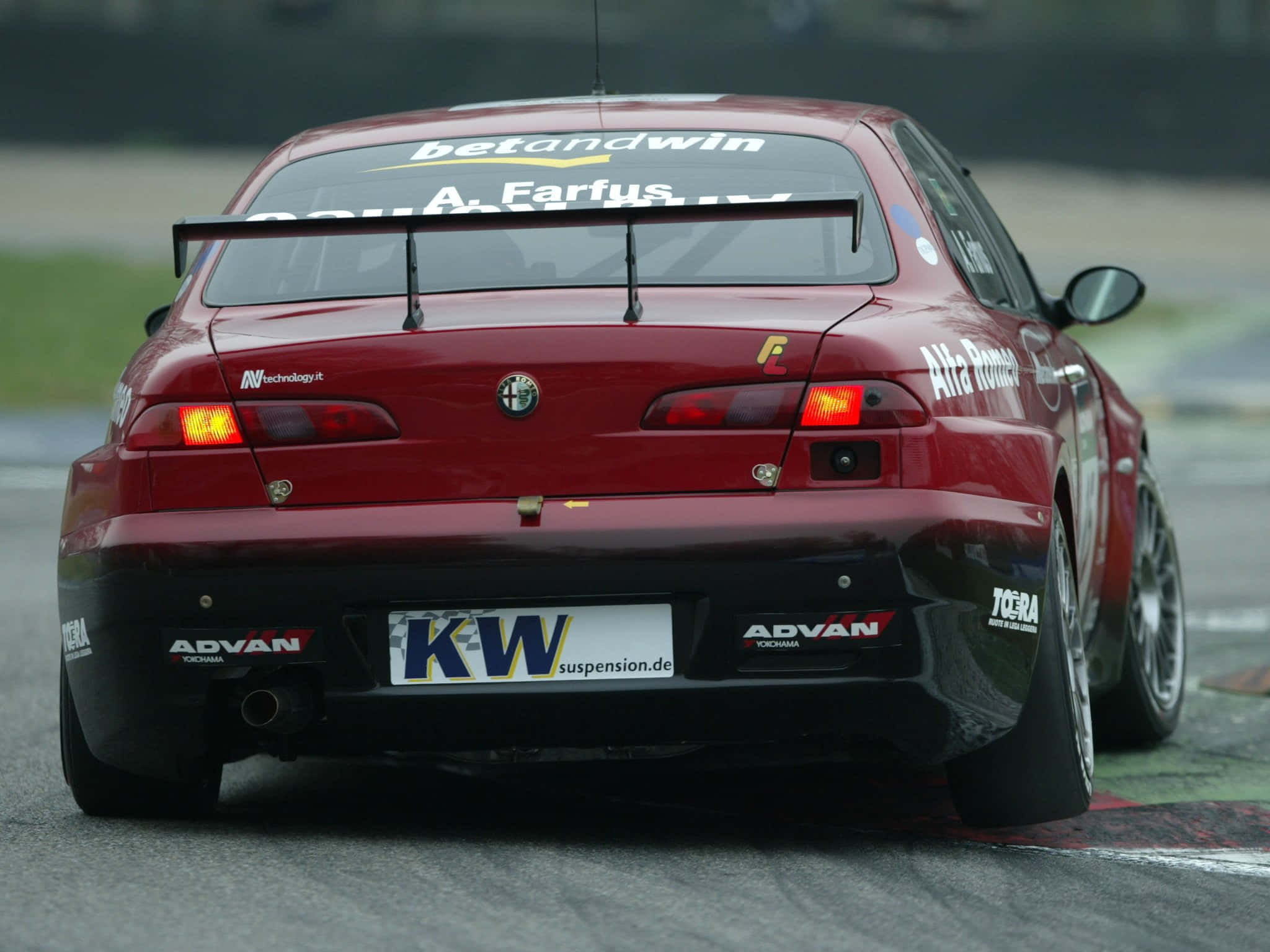 Alfa Romeo 156 桌布 壁紙 — 一輛帶有贊助商貼紙的紅色愛快羅密歐賽車，在潮濕的賽道上高速行駛，呈現動態模糊效果和發光的尾燈。