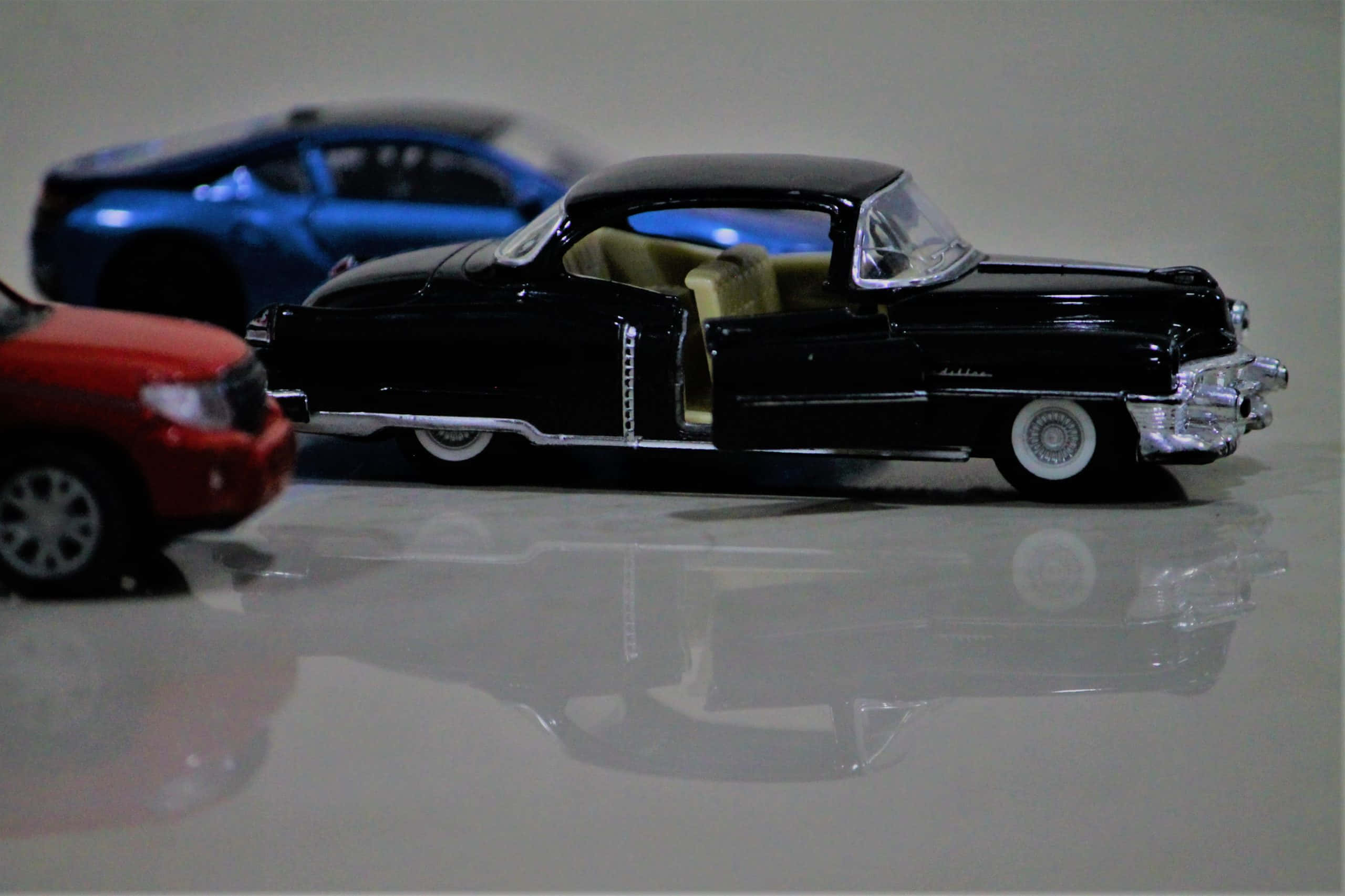 Car Model 桌布 壁紙 — 一輛帶有鍍鉻細節和米色內飾的光澤黑色復古玩具車放在反光表面上，旁邊是一輛藍色和紅色的玩具車。