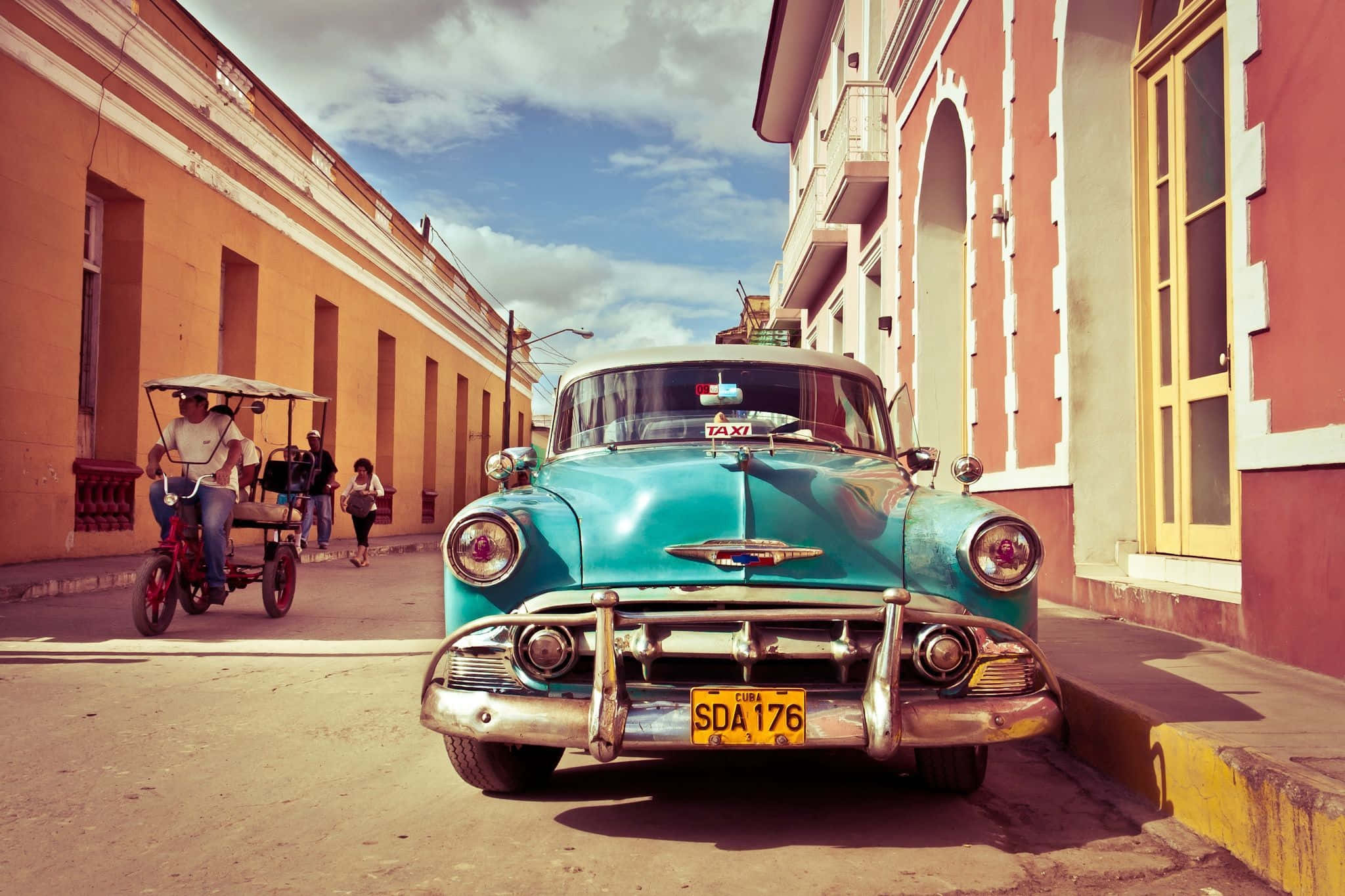 Cuba 桌布 壁紙 — 一輛帶有鍍鉻細節的復古青綠色出租車停在古巴陽光明媚的街道上，兩旁是色彩繽紛的殖民時期建築。