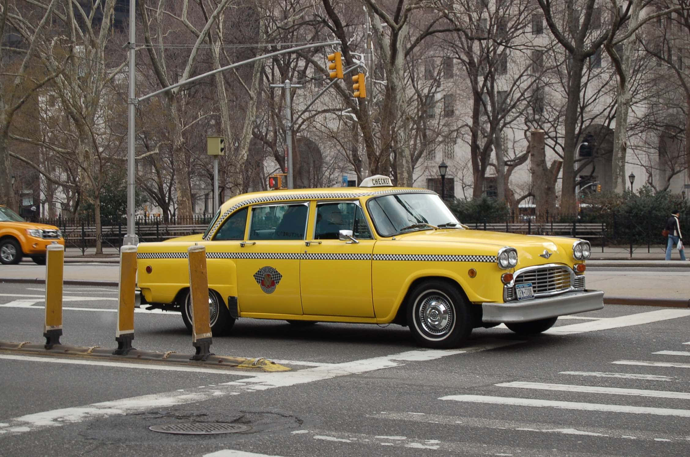 Yellow Cab 桌布 壁紙 — 一輛帶有黑色棋盤格條紋的復古黃色出租車在佈滿光禿樹木的城市交叉口等待。