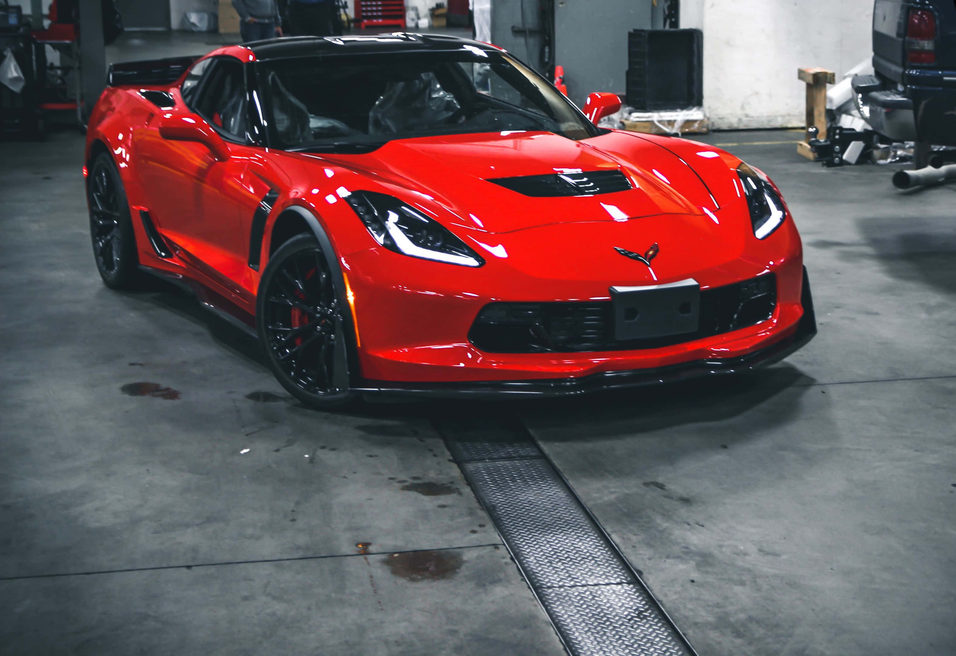 Chevrolet Corvette Z06 桌布 壁紙 — 一輛帶有黑色裝飾的亮紅色Corvette跑車停在光線昏暗的車庫裡，車庫有混凝土地板和散落的工具。
