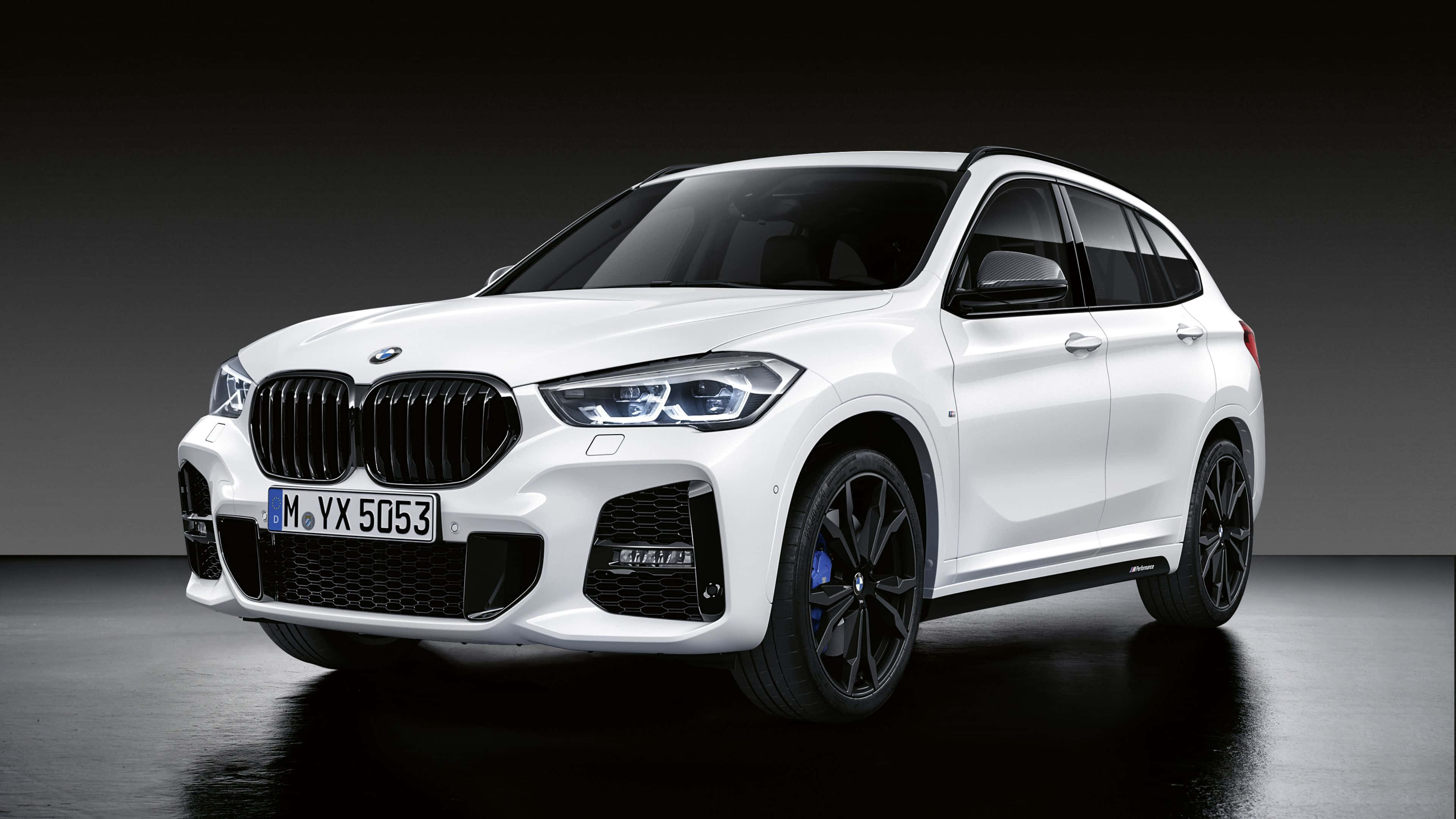 Bmw X1 桌布 壁紙 — 一輛帶有黑色飾件和藍色制動卡鉗的純白色BMW X1 SUV，在時尚的攝影棚中以戲劇性燈光展示。