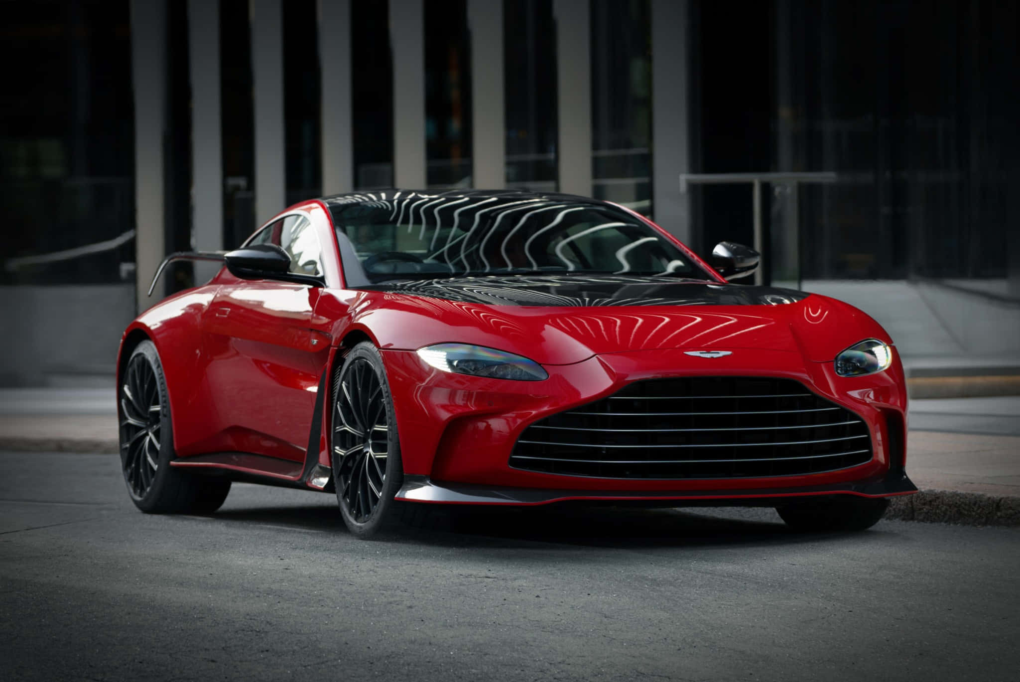 Aston Martin Vantage 桌布 壁紙 — 一輛帶有黑色飾邊的亮紅色Aston Martin跑車在黃昏時停泊在城市的街道上。