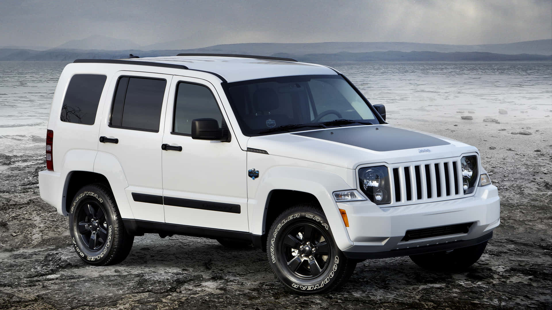 Jeep Liberty 桌布 壁紙 — 一輛帶有黑色飾邊的白色Jeep Patriot SUV停在泥濘的海岸線上，天空多雲，遠處有山巒。