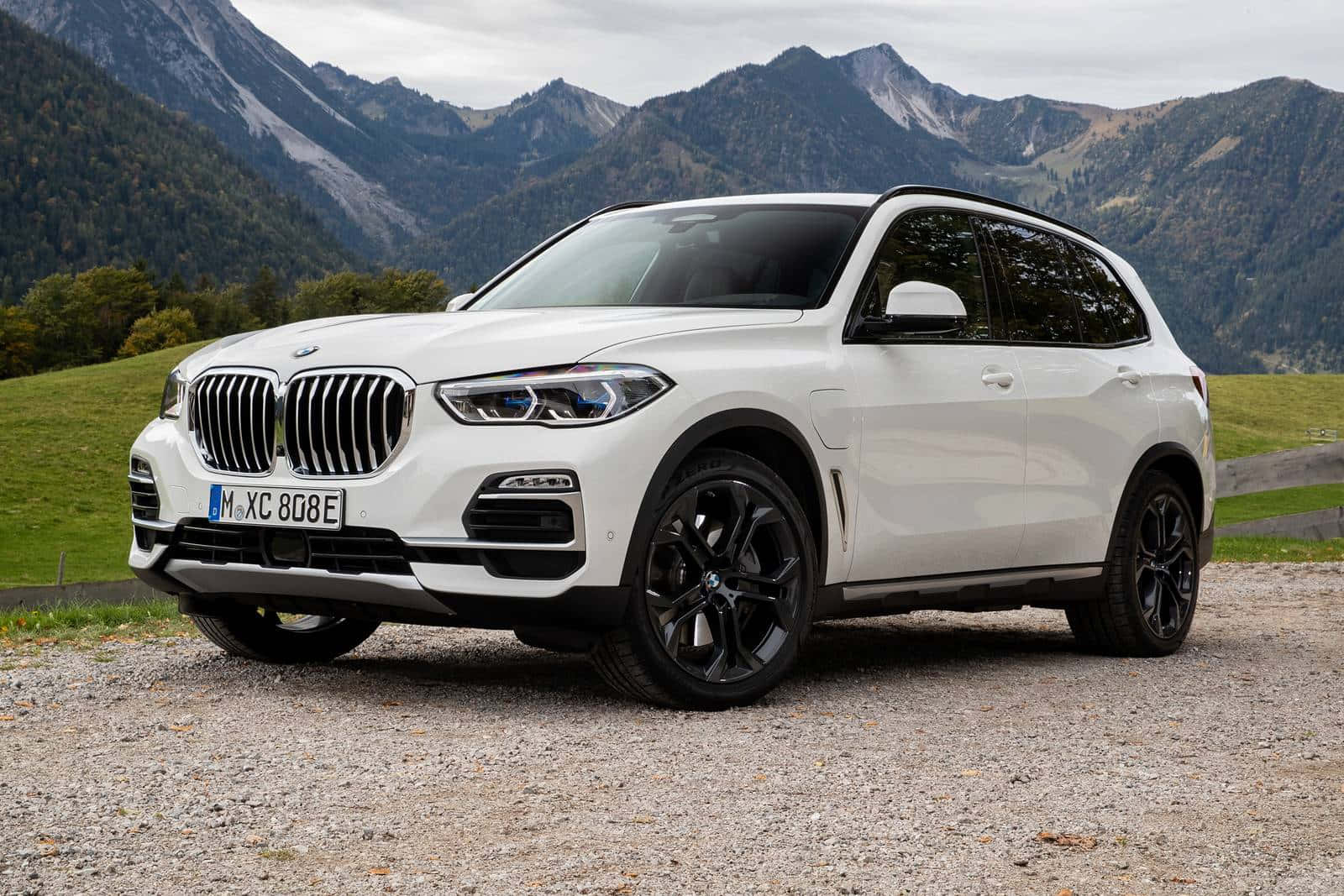 Bmw X5 桌布 壁紙 — 一輛帶有黑色飾邊的純白色BMW X5 SUV停泊在碎石上，背景是崎嶇的山脈和綠色的山丘。