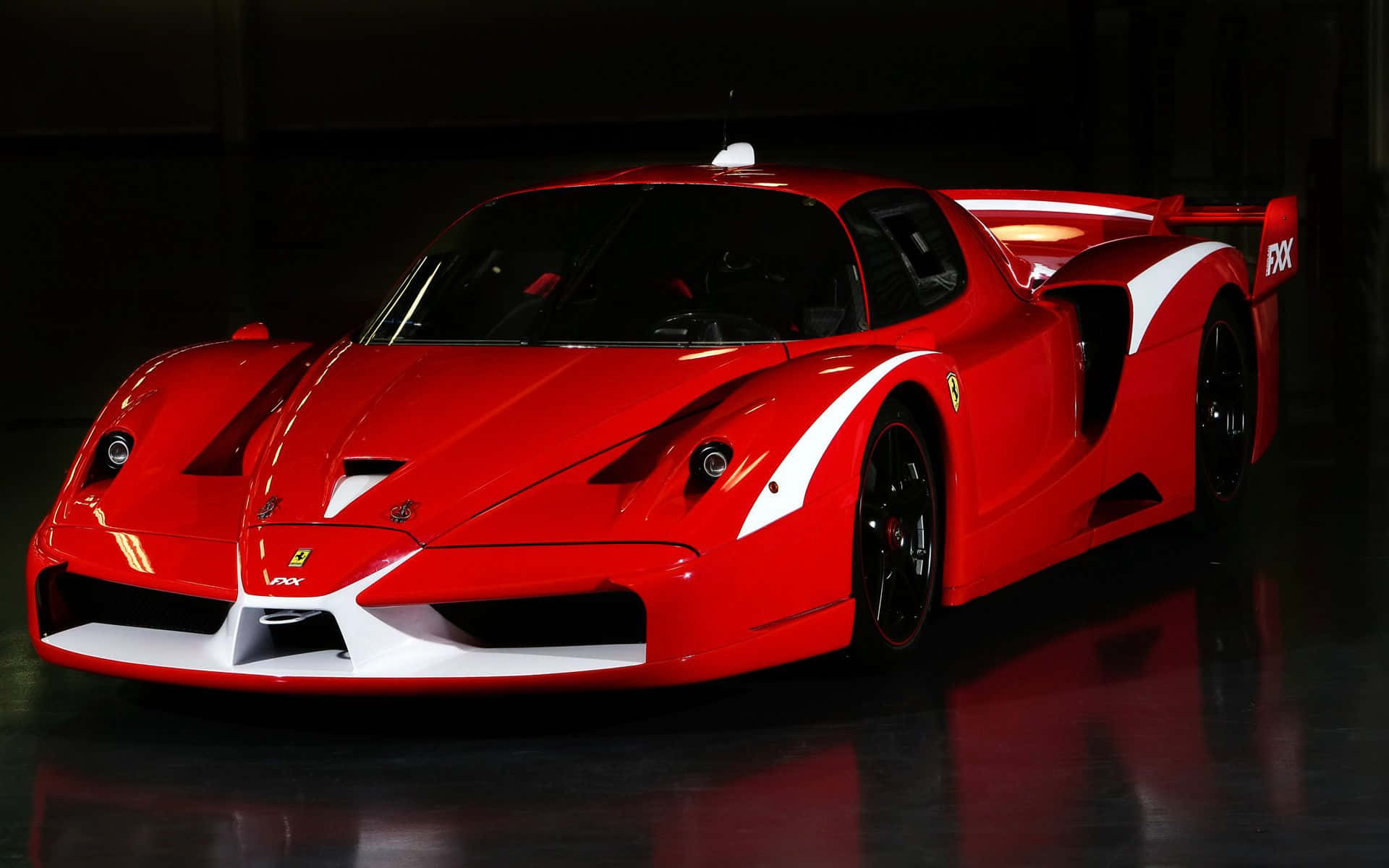 Ferrari Enzo 桌布 壁紙 — 一輛引人注目的紅色法拉利FXX賽車帶有白色點綴，在反光地板上的工作室燈光下閃閃發光。