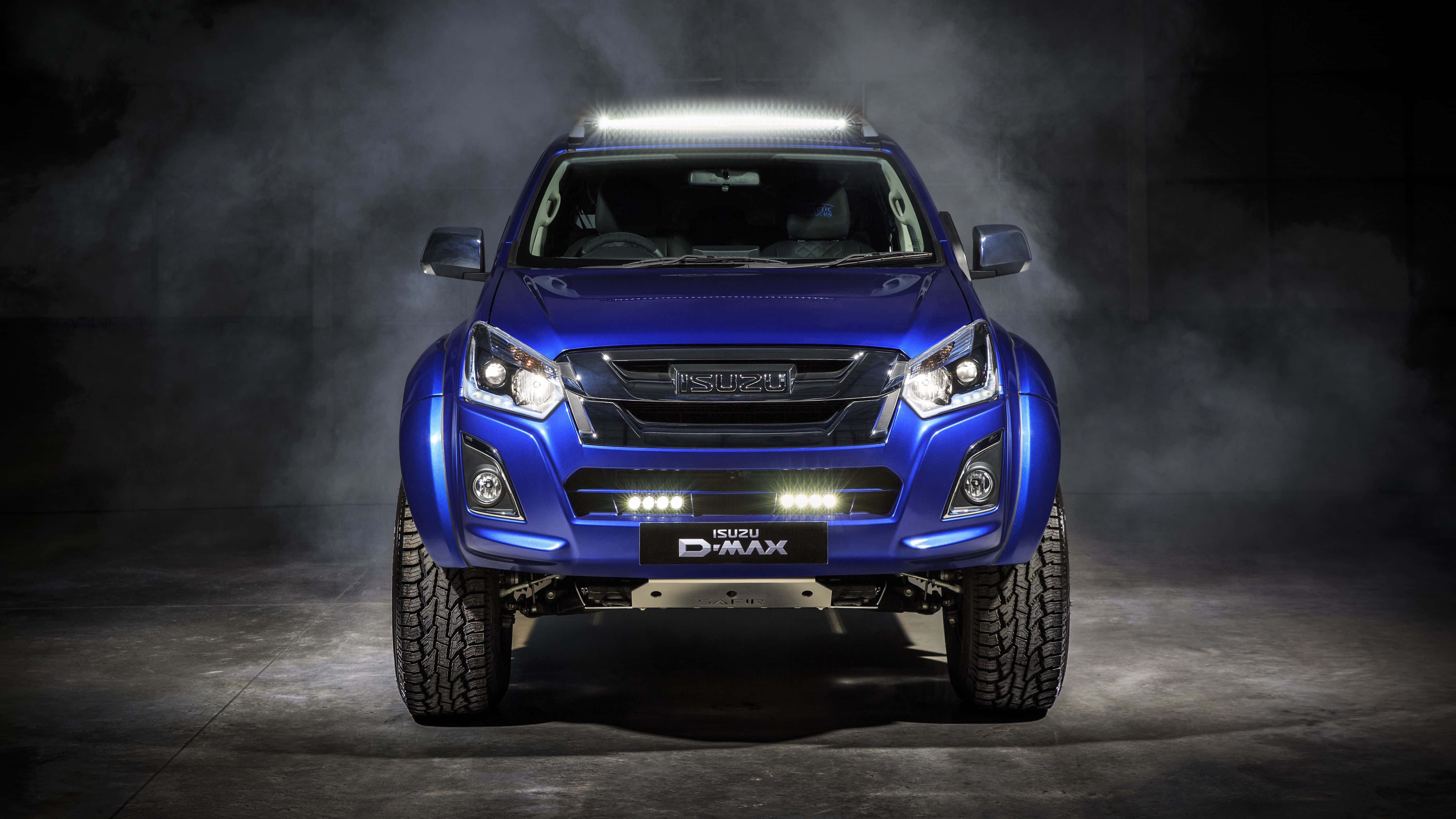 Isuzu 桌布 壁紙 — 一輛引人注目的藍色Isuzu D-MAX皮卡車在戲劇性的攝影棚燈光下向前，煙霧在其堅固的輪胎周圍旋轉。