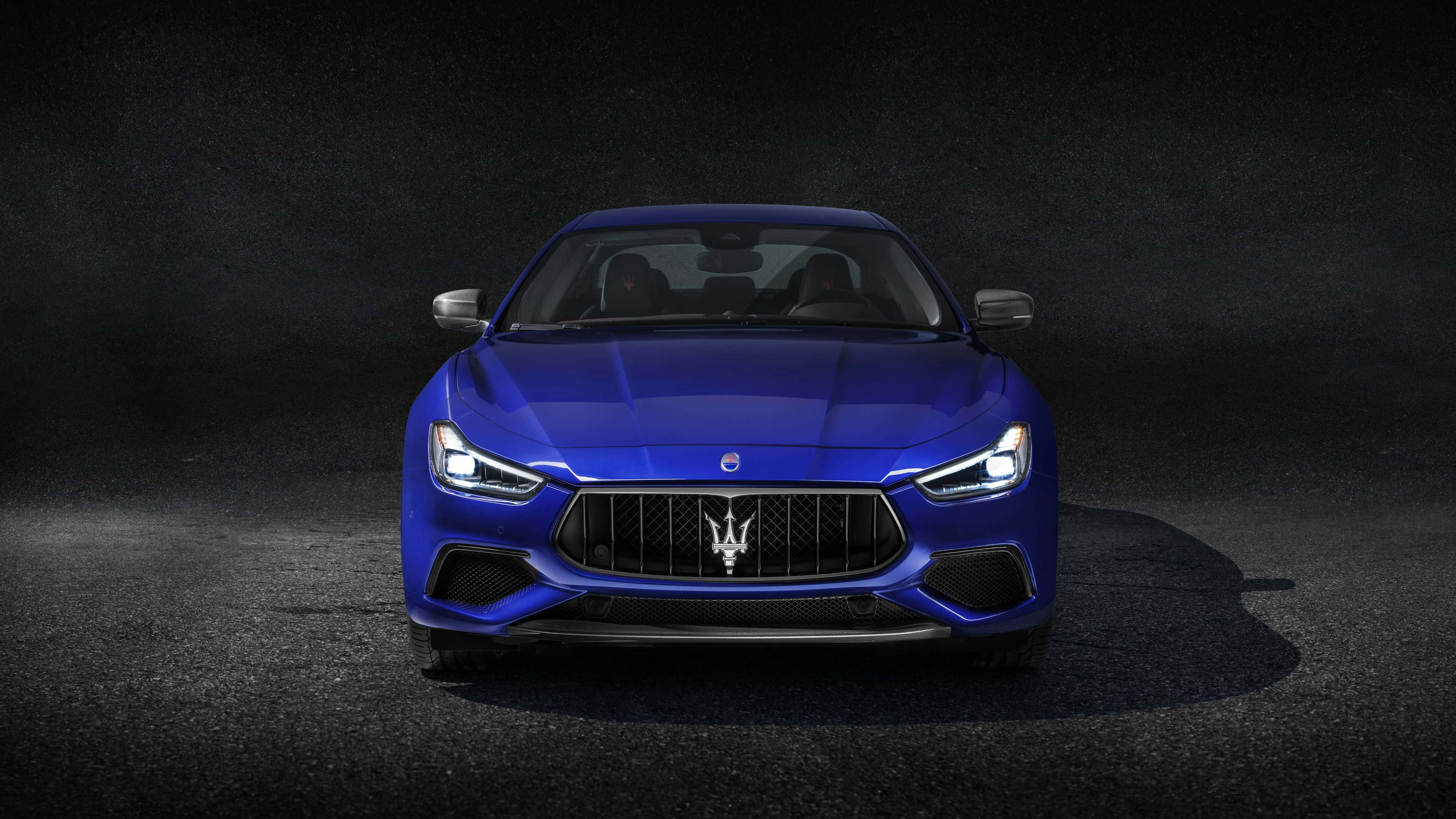 Maserati Ghibli 桌布 壁紙 — 一輛引人注目的藍色瑪莎拉蒂跑車在戲劇性的聚光燈下，在深色紋理背景上閃閃發光。