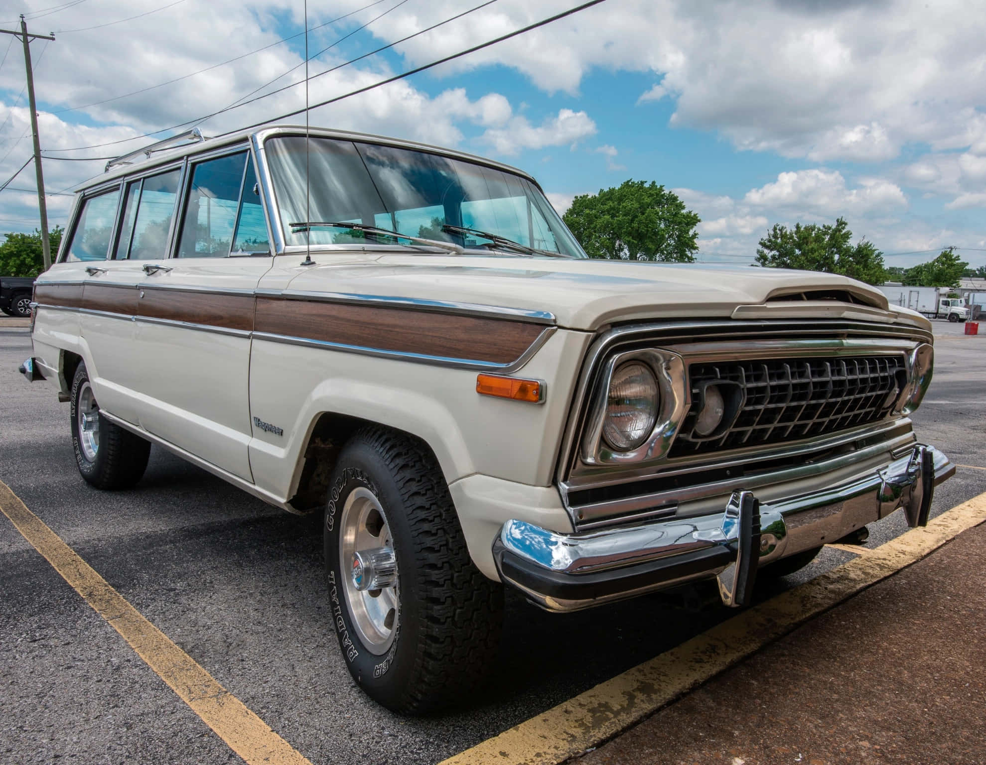 Jeep Wagoneer 桌布 壁紙 — 一輛復古奶油色和木紋的Jeep Wagoneer停在停車場，天空部分多雲。