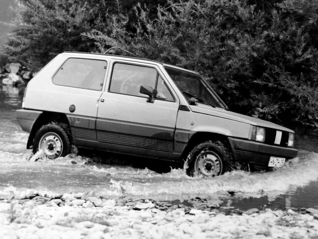 Fiat Panda 桌布 壁紙 — 一輛復古小型車在黑白鏡頭中濺起水花，穿過被茂密樹葉環繞的淺石溪流。