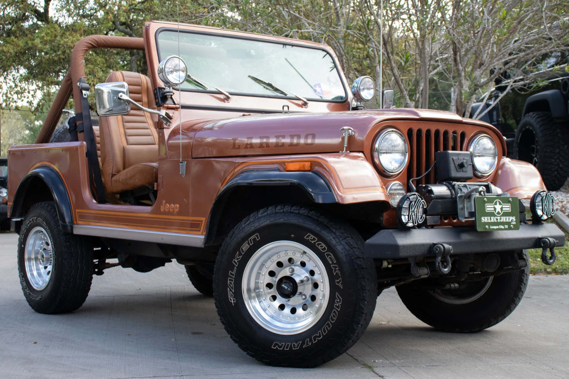 Jeep Cj 桌布 壁紙 — 一輛復古棕色Jeep Wrangler，配備米色內飾和鍍鉻飾邊，停泊在樹木環繞的混凝土車道上。