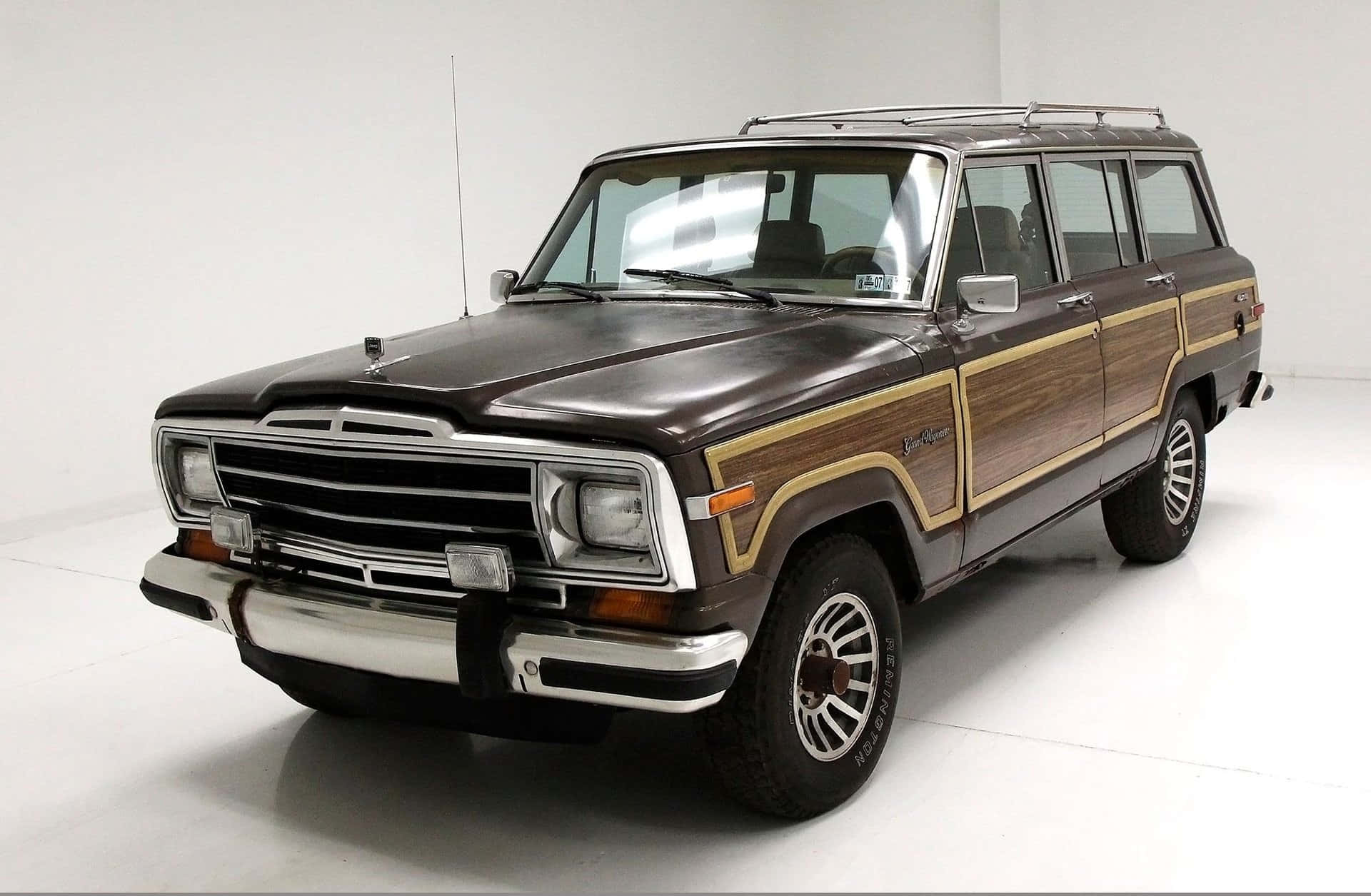 Jeep Wagoneer 桌布 壁紙 — 一輛復古棕色木紋車身的Jeep Wagoneer，帶有鍍鉻飾邊和車頂行李架，停在明亮的白色攝影棚內。