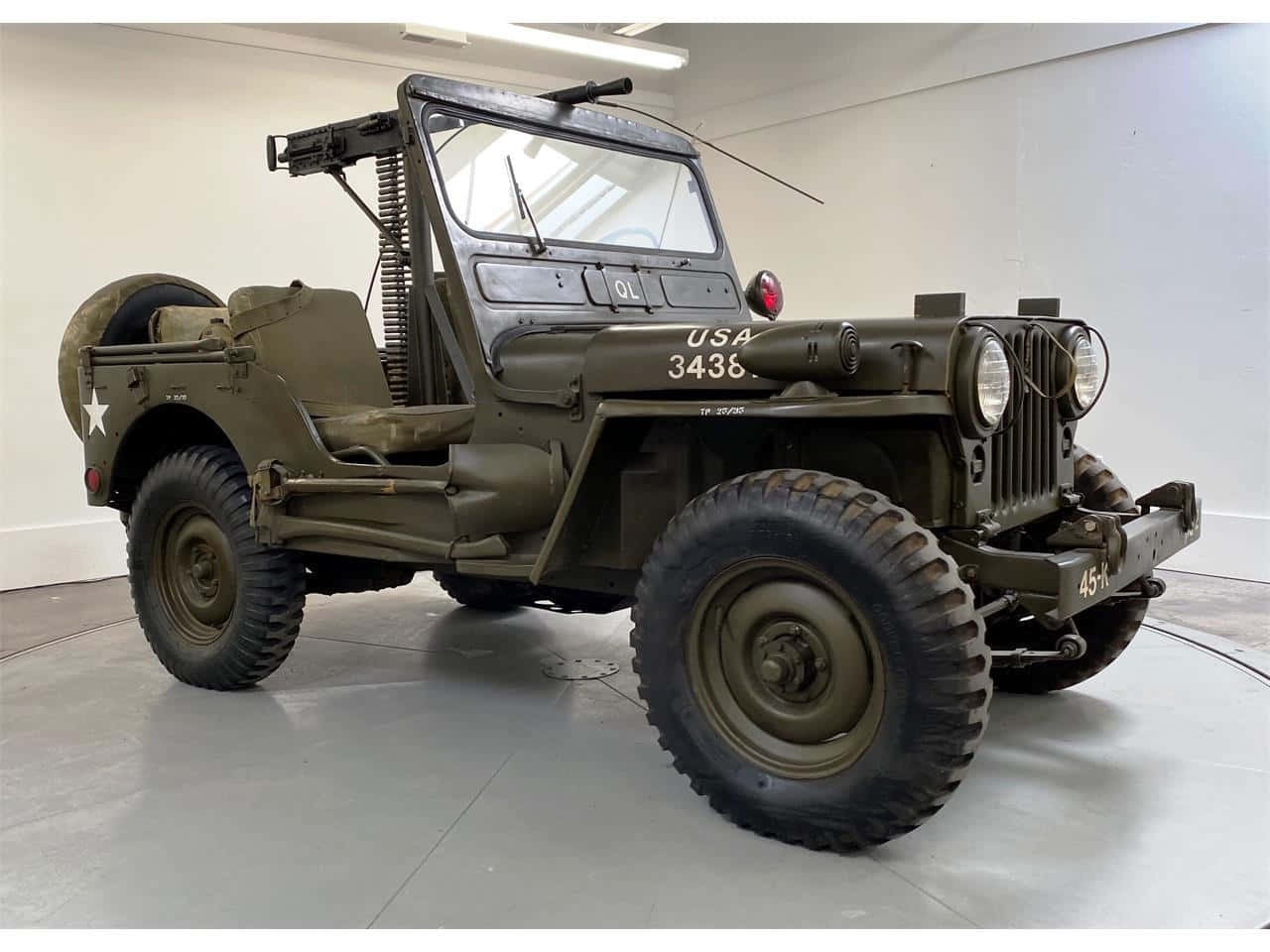 Jeep Willys 桌布 壁紙 — 一輛復古橄欖綠軍用吉普車，配有機槍和星形徽章，展示在乾淨的室內車庫中。