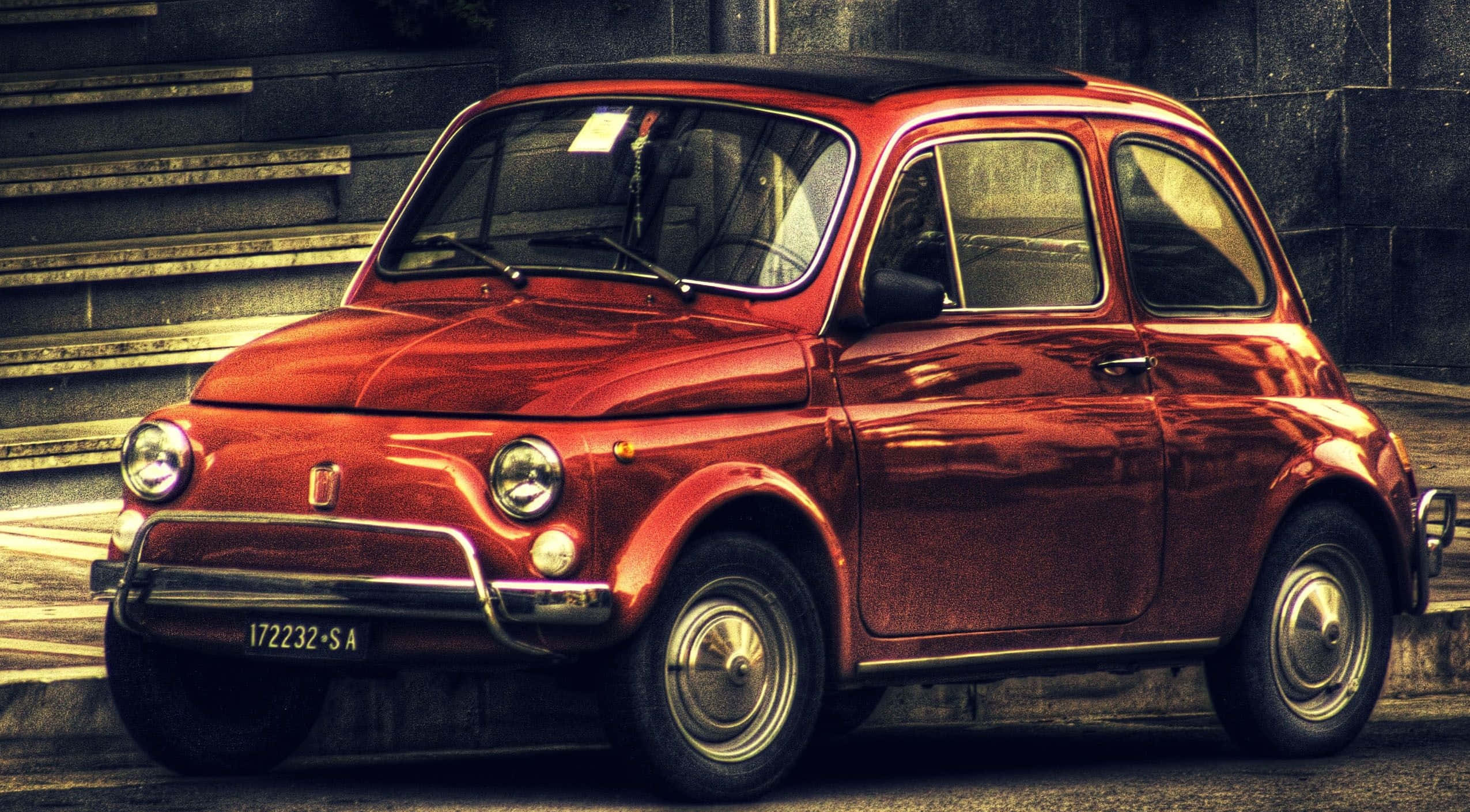Fiat 500l 桌布 壁紙 — 一輛復古紅色菲亞特500停泊在陽光普照的城市街道上，後面有石階。