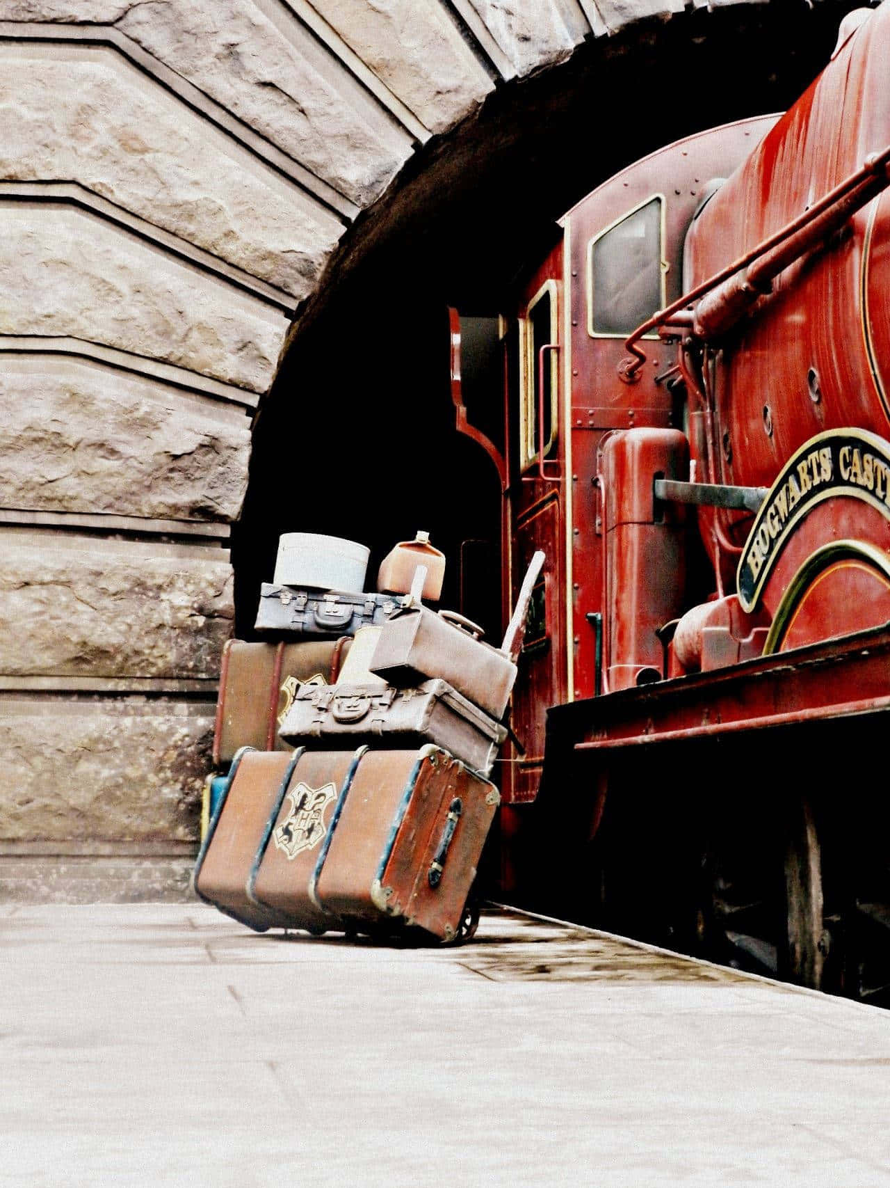 Hogwarts Express 桌布 壁紙 — 一輛復古紅色蒸汽火車從石隧道中駛出，旁邊堆疊著一堆破舊的皮革行李箱。