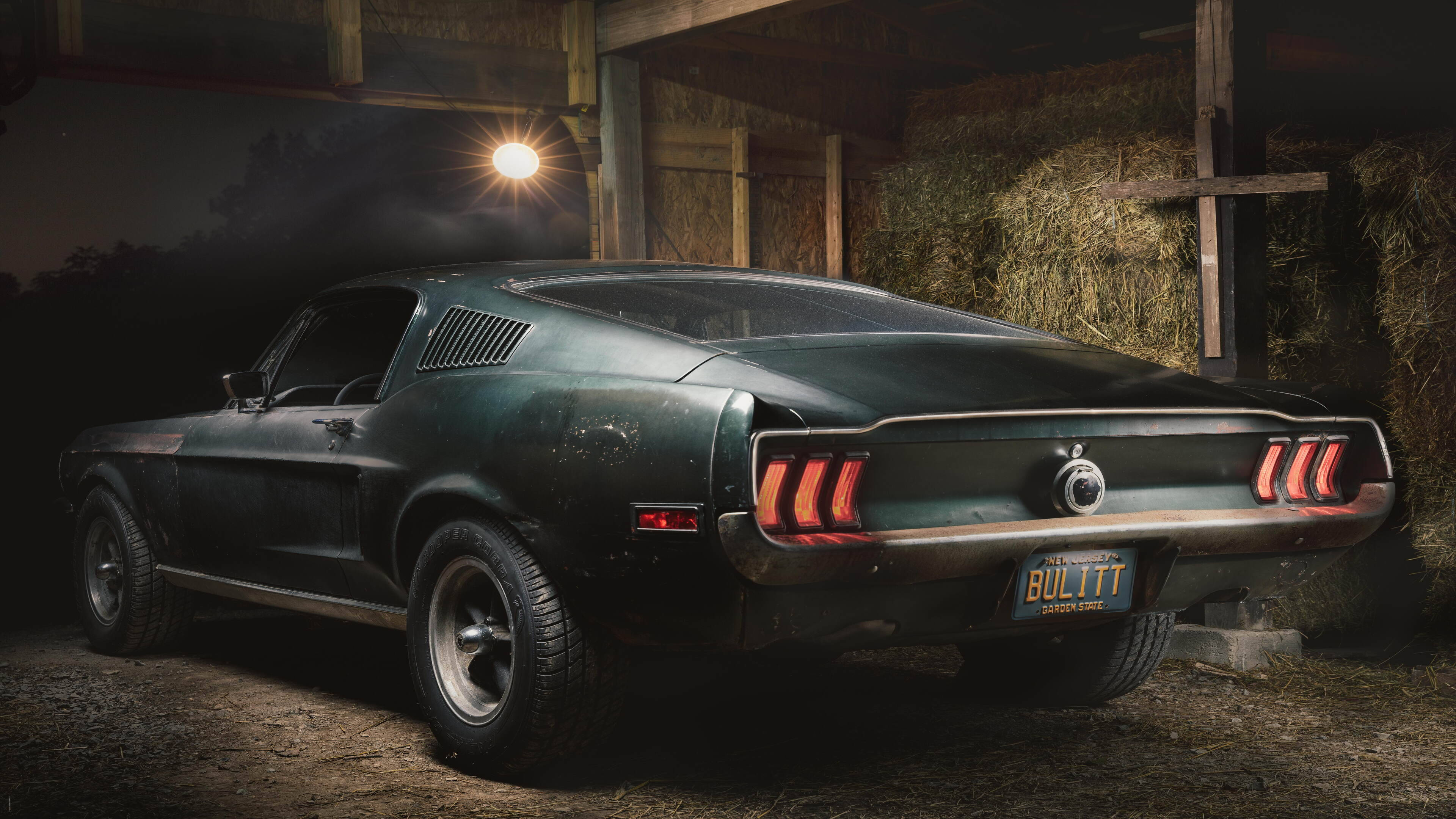 mustang HD 桌布 壁紙 — 一輛復古綠色Mustang Bullitt在鄉村木棚中，於單一穀倉燈光下與乾草捆旁閃閃發光。