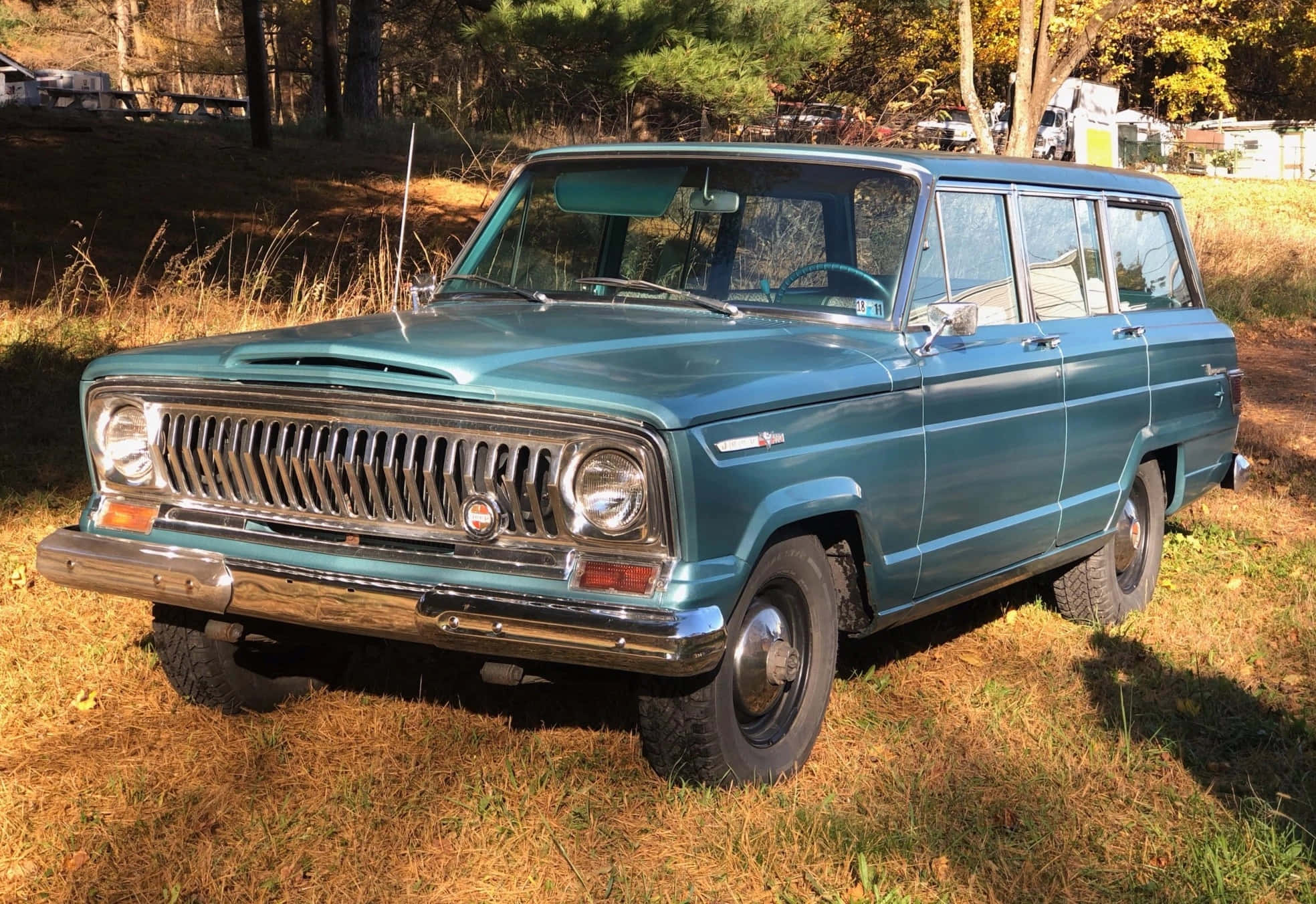 Jeep Wagoneer 桌布 壁紙 — 一輛復古青綠色旅行車停在乾草上，周圍是秋樹，金色陽光投下長長的影子。